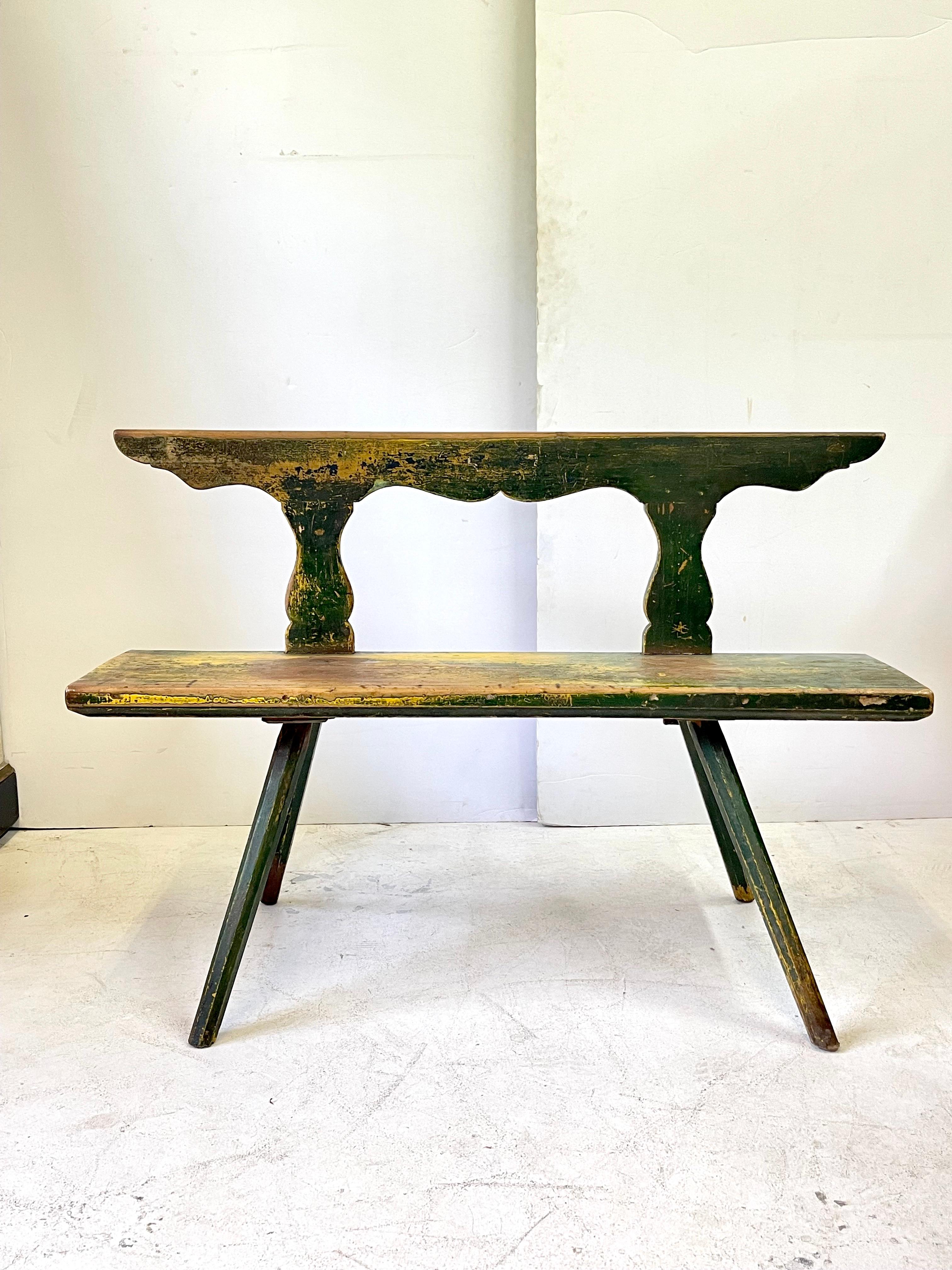 19th Century Italian rustic refrectory settee having a beautifully shaped back, long rectangular bench seat with primitive joinery, and dramatically splayed legs. The settee is now mostly in a dark green paint with a yellow undercolor and the