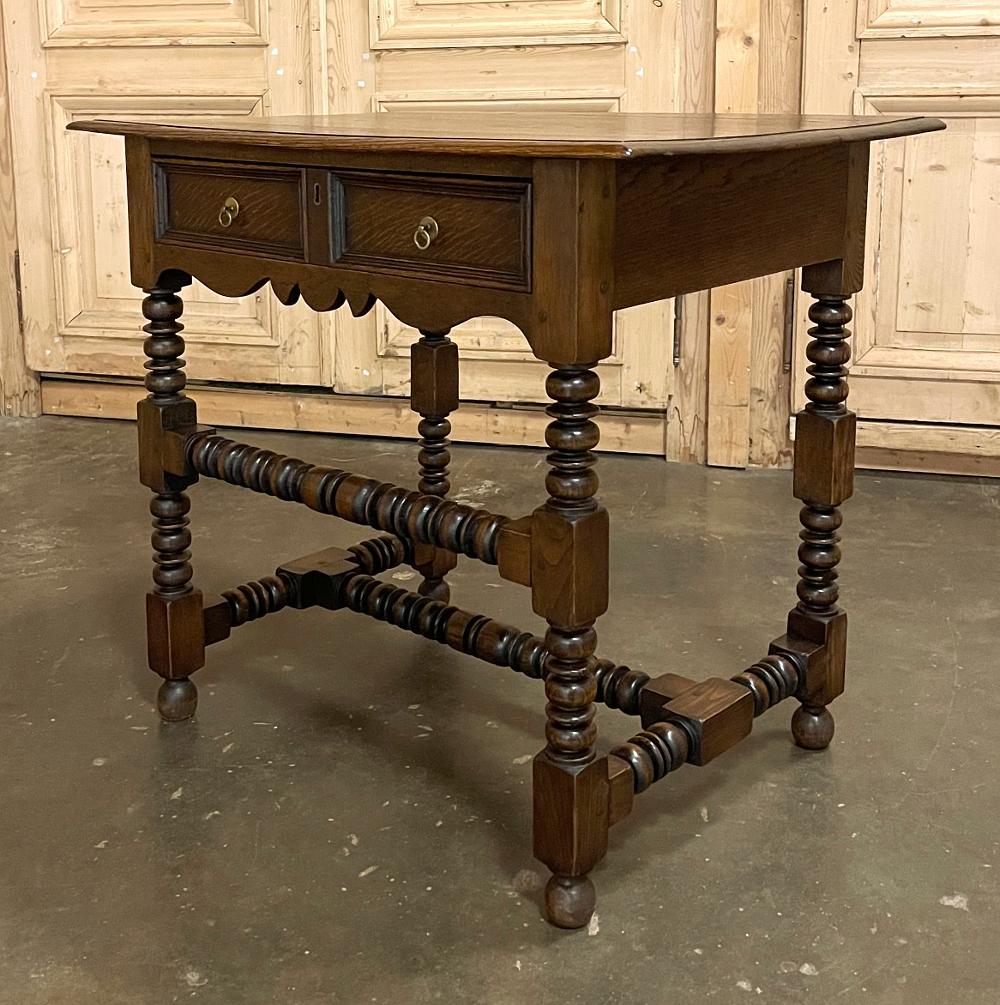 19th century rustic Jacobean end table was hand-crafted from solid old-growth oak, and features a plank top with two tailored drawers with brass ring pulls framed by a scrolled apron. Intricately turned spool-pattern legs and stretchers comprise the