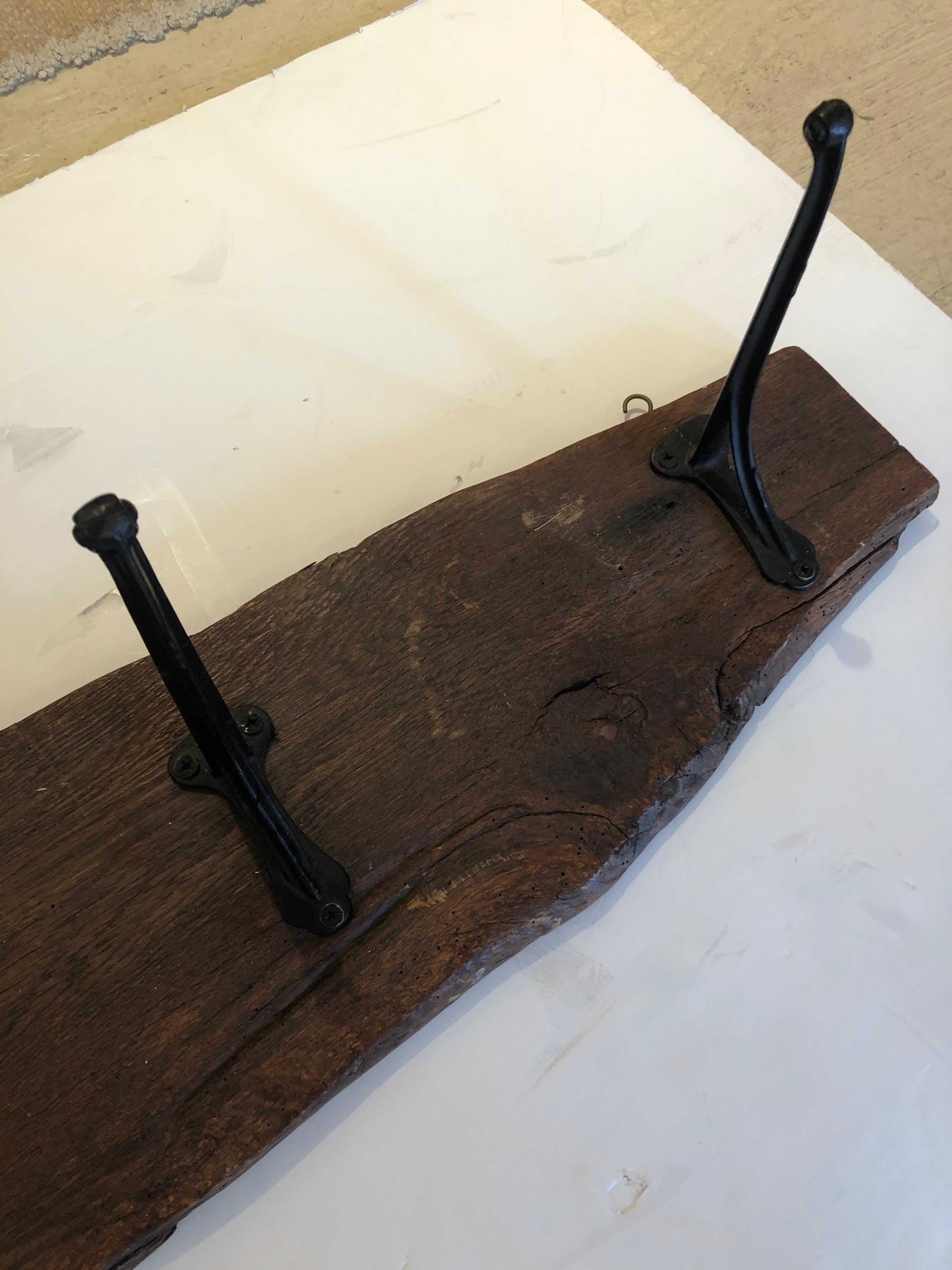 A functional and rustic antique hanging wall coat hanger made from a live edge hunk of impressive wood and having authentic original wrought iron hooks.