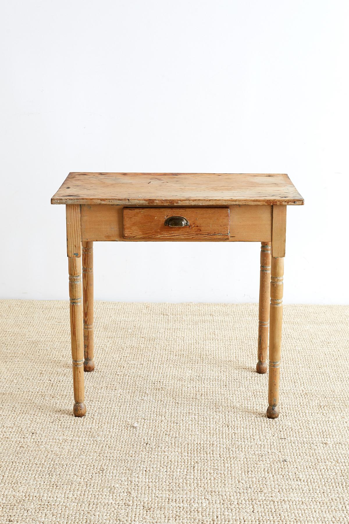 19th century rustic pine farmhouse table or work table. Features a simple provincial style construction with elegant turned pine legs and round feet. Fronted by a small drawer with a brass pull. Lovely distressed patina with good joinery.

Offered