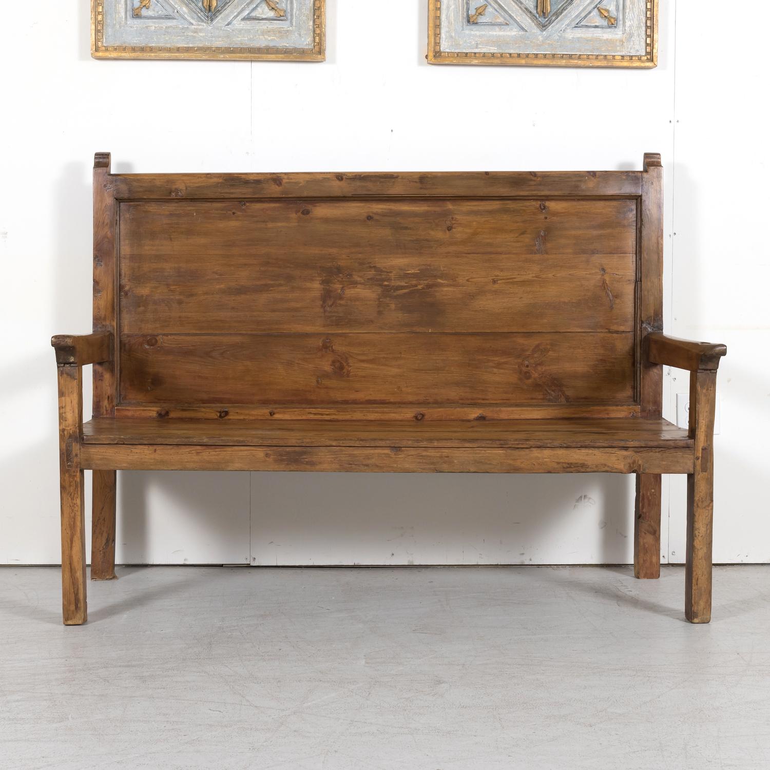 19th Century rustic Spanish Colonial hall bench handcrafted in the Catalan region of solid pine, having a high back with sculptural posts and plank seat raised on square legs, circa 1880s. This handsome bench has aged and weathered to a beautiful