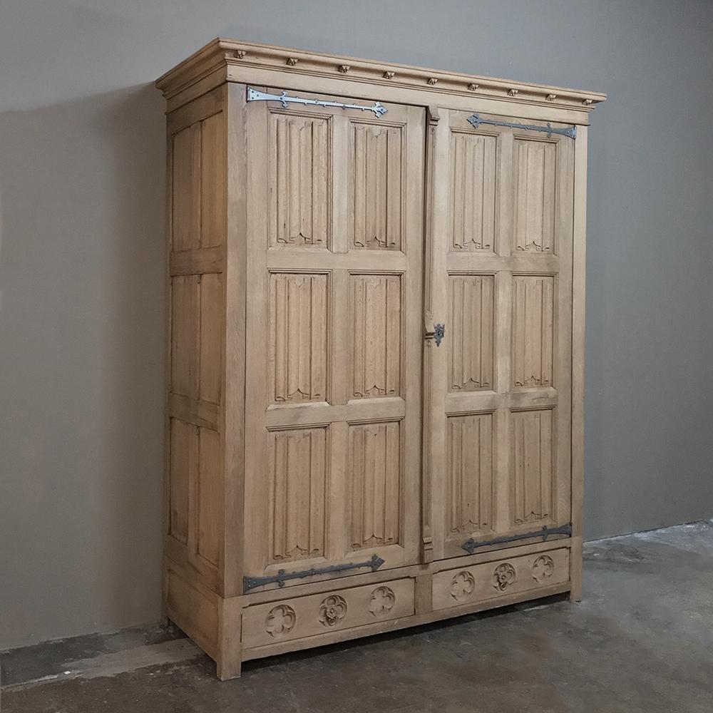 19th century rustic stripped oak Gothic armoire was handcrafted from solid oak and features tailored lines enhanced by 12 linenfold panels on the doors mounted with decorative iron strap hinges, plus a pair of drawers below carved with