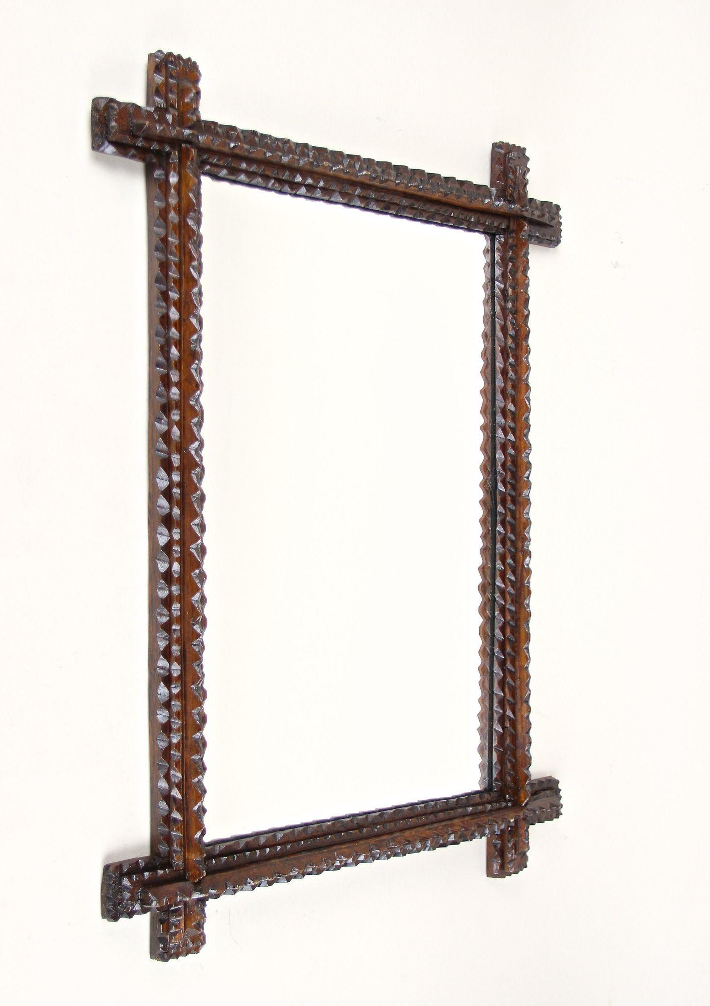 Exceptional looking rustic 19th century Tramp Art mirror out of Austria. This fantastic rustic wall mirror from around 1870 convinces by its great variety of chip carvings. Slightly protruding corners and the dark brown stained frame makes this