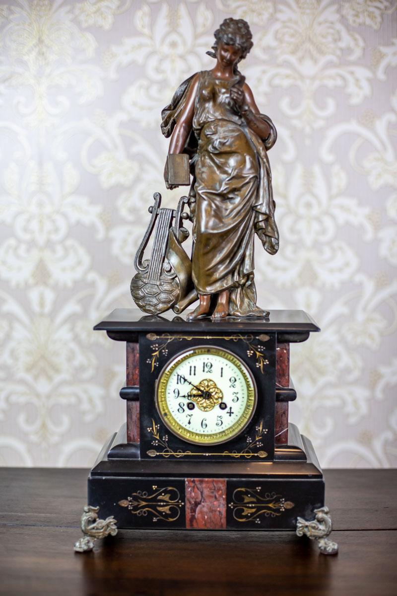 We present you a mantel clock with two candelabras.
The case of the clock is made of two types of marble and topped with a brass figurine of a muse.
Furthermore, the clock face, with Arabic numbers, is glazed, closed in a brass frame.
The tension