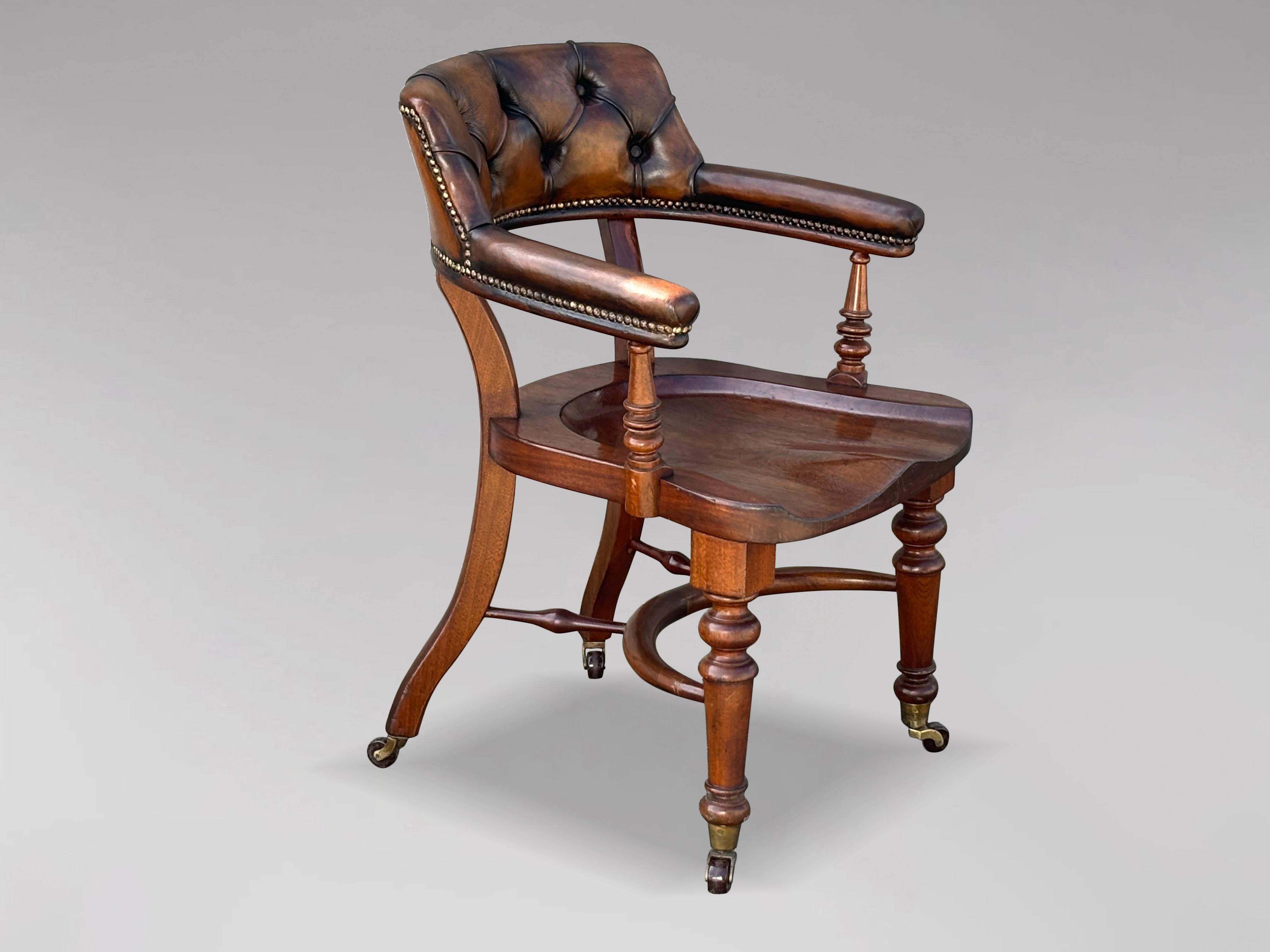 A fine quality 19th century English Victorian period saddle seat desk chair, constructed of solid mahogany with a brown upholstered backrest and armrests, circa 1880. The mahogany office chair benefits from a curved, deep-buttoned padded backrest,