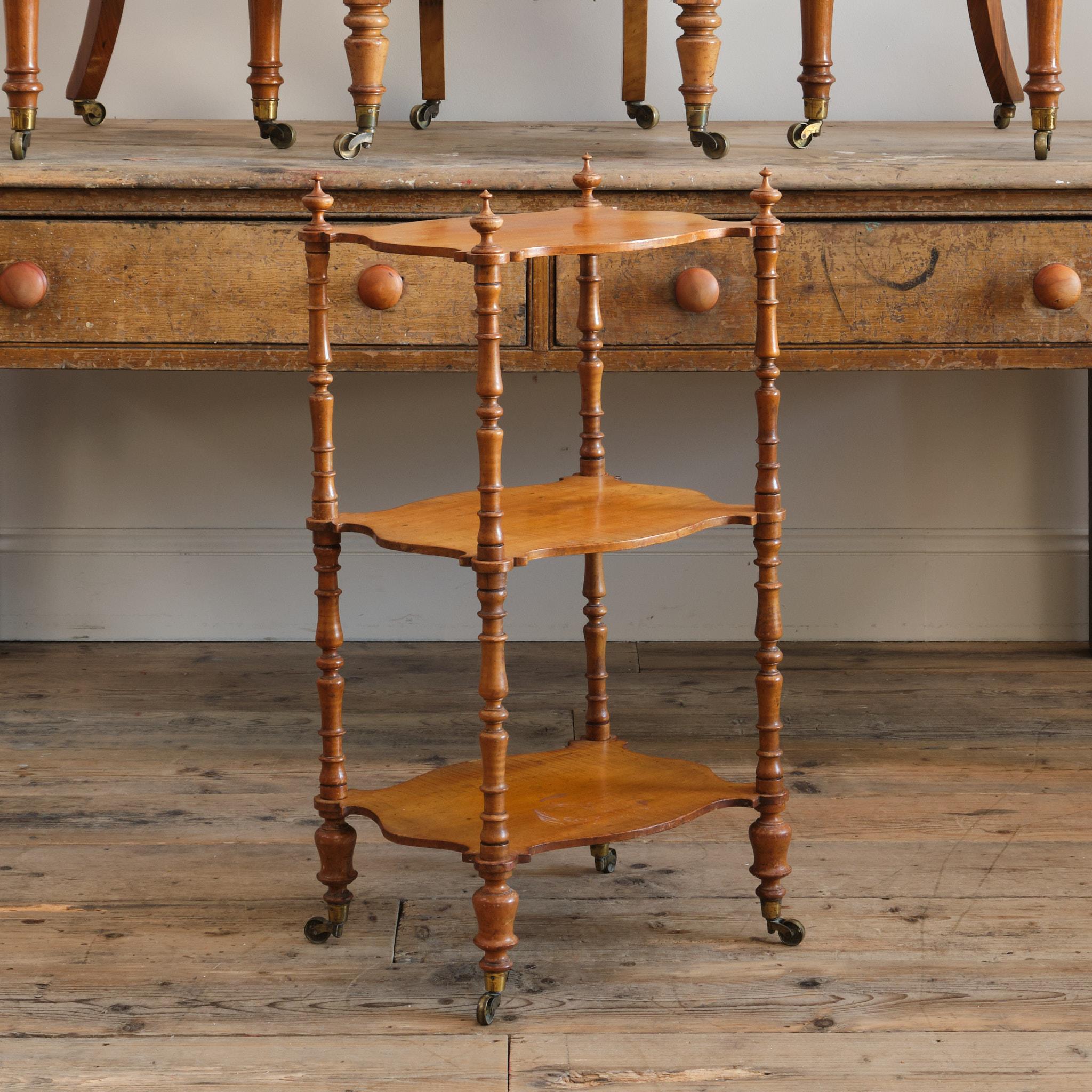A mid 19th century whatnot. The shaped shelves are nicely figured satin birch with turned spindle uprights and raised on 4 turned legs with the original casters. The whole disassembles into flat pack form by unscrewing the turned wooden screws and
