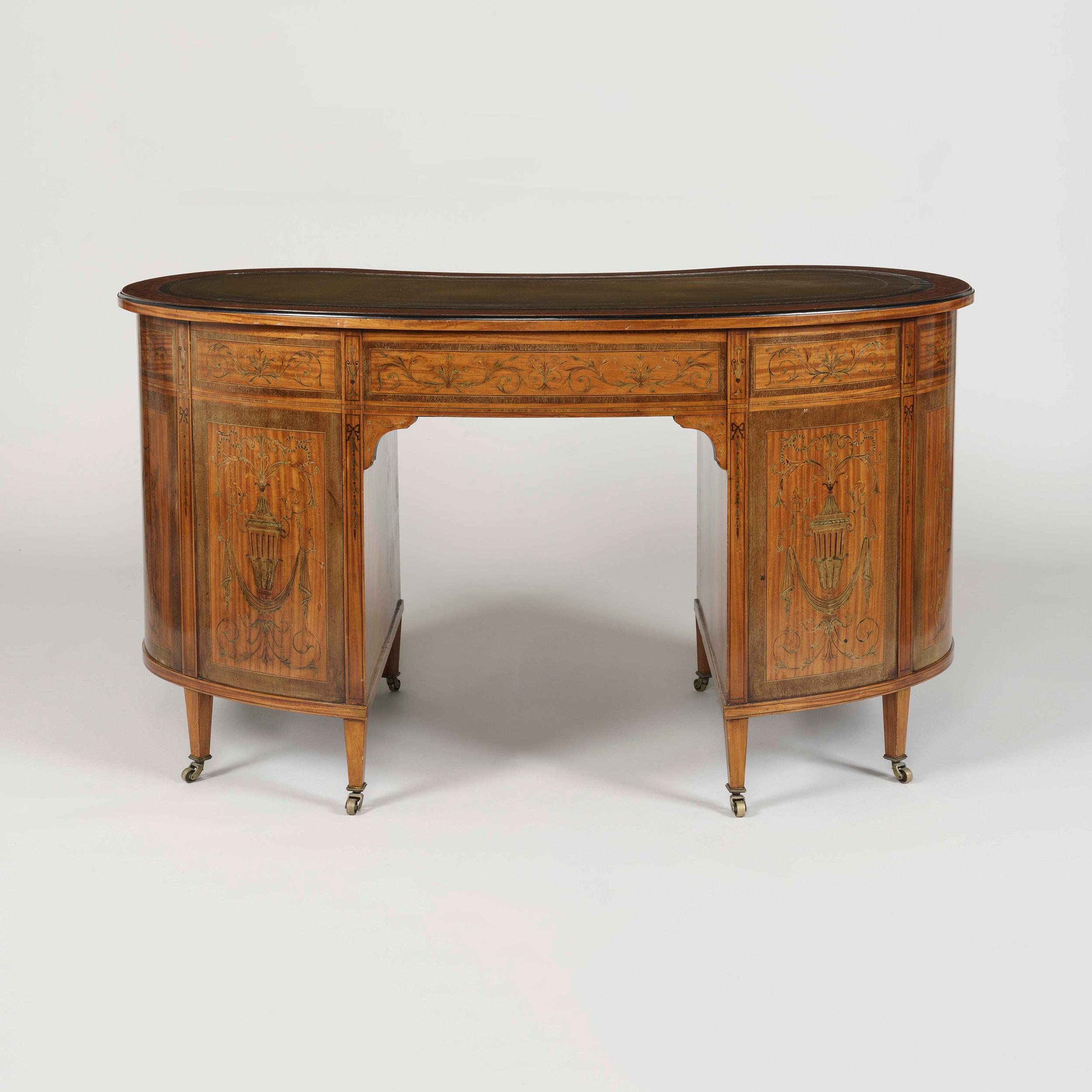 A satinwood and marquetry kidney-shaped writing desk
in the manner of Maple & Co

The moulded and tooled leather inset top above an arrangement of nine drawers, inlaid throughout with engraved foliate scrolls, and urns, within ebonized stringing