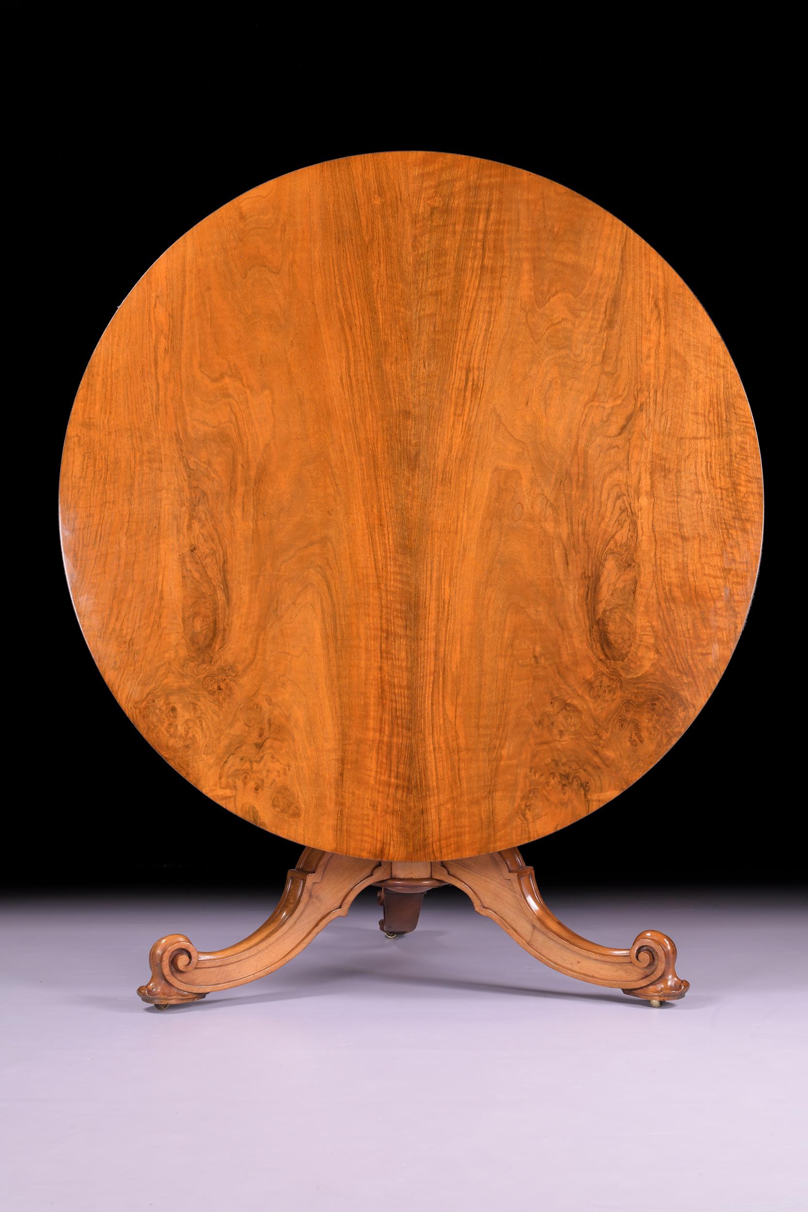 Une très belle table centrale en bois de satin du 19ème siècle par Holland & Sons. La table est en bois de satin finement figuré avec un plateau circulaire basculant au-dessus d'une colonne balustre avec trois pieds sculptés en S et en feuilles,