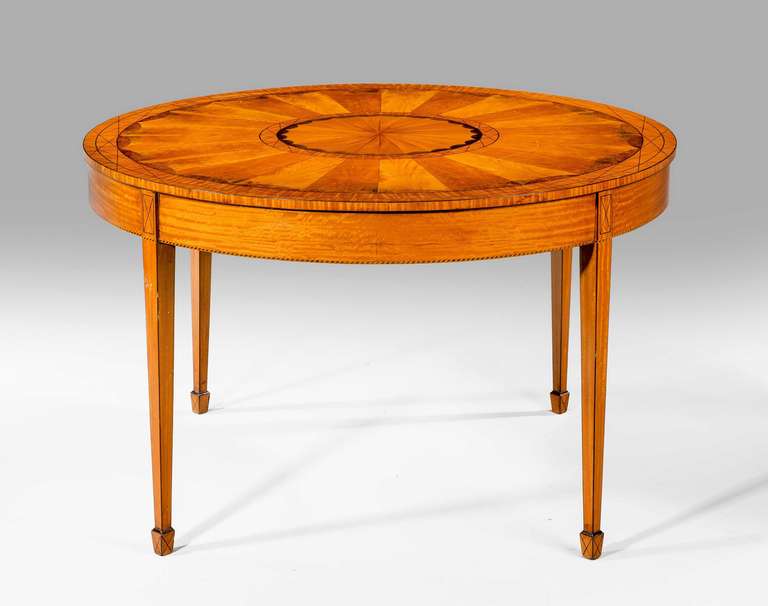 A 19th century satinwood circular centre table with an elaborate radiating sunburst top, mahogany edging on square tapering supports.

 