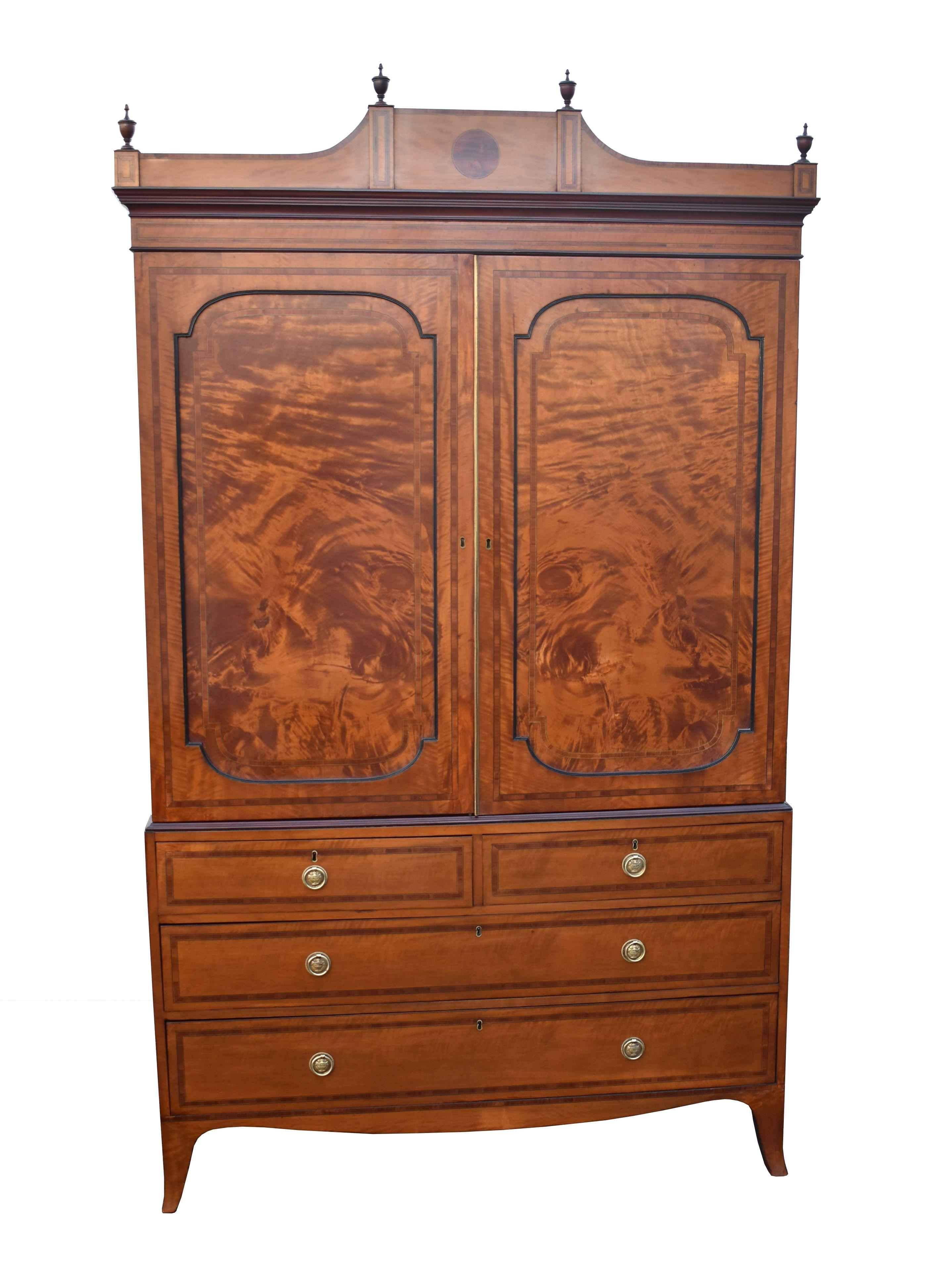 For sale is a top quality 19th century satinwood linen press, having an architectural pediment, urn finials, and two well figured panel doors enclosing original linen trays. The base is comprised of two short over two long drawers, banded with