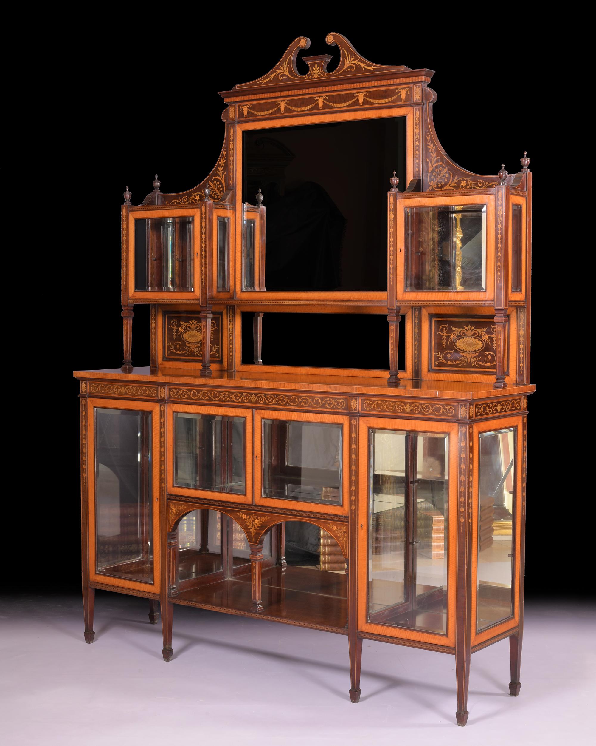 An outstanding late 19th century satinwood, mahogany and marquetry inlaid side cabinet attributed to Wright and Mansfield, the raised mirrored back with swan neck pediment, bevelled plates and glazed display compartments, the base with glazed