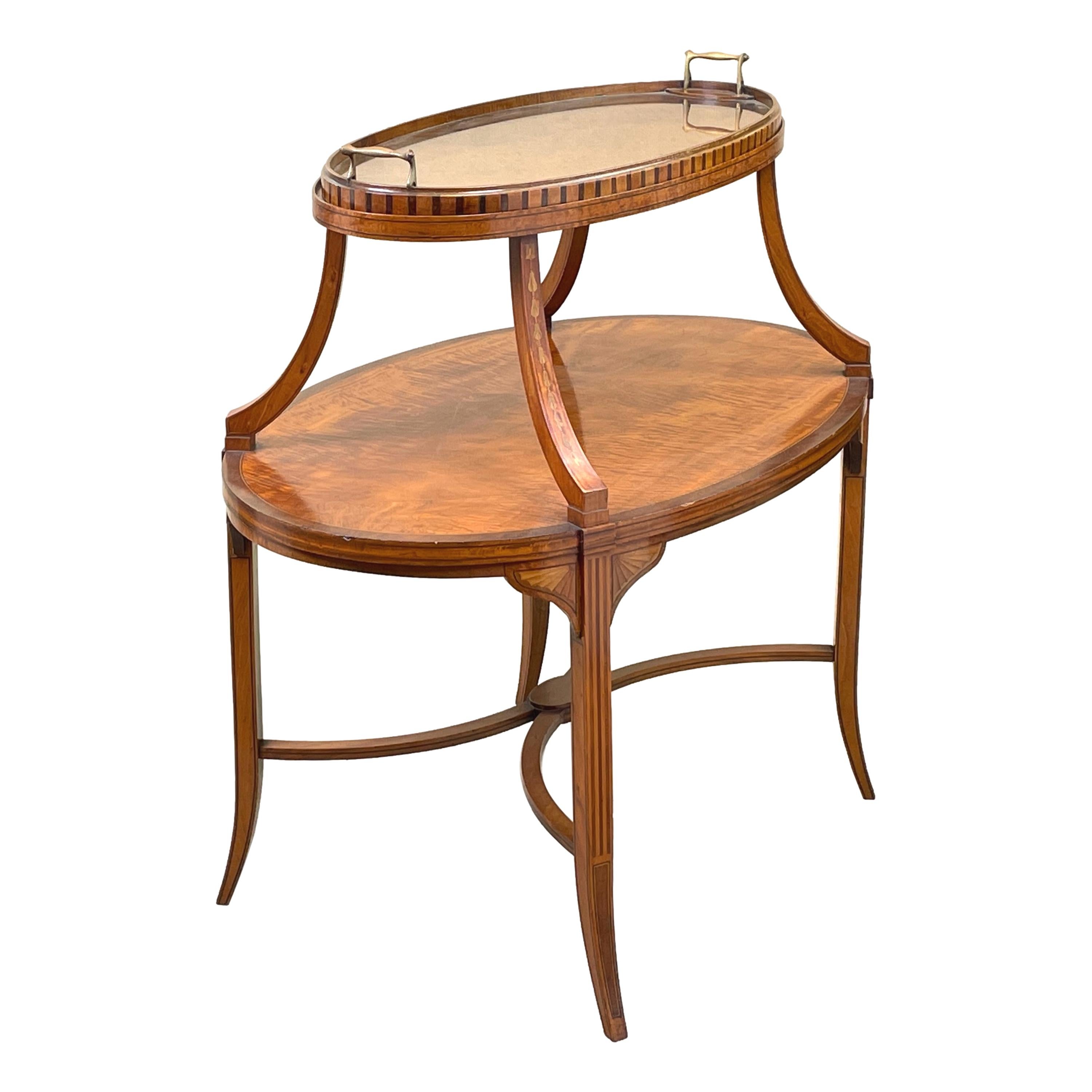 A fine quality late 19th century satinwood oval two tier etagere, or dumbwaiter, having removable lift off glass tray top and superbly figured veneers with crossbanded and inlaid decoration raised on four elegant splayed legs united by central