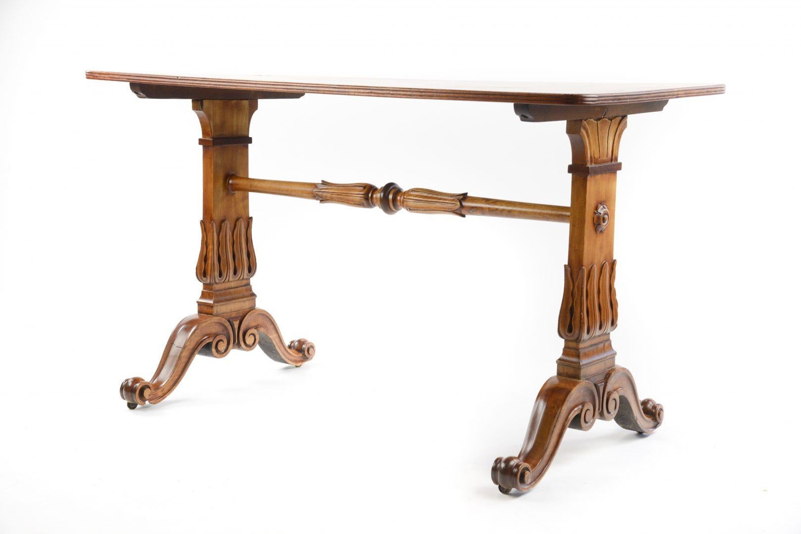 A 19th century satinwood rectangular library table, with stiff leaf carved trestle ends united by pole stretcher, on scrolling down-swept supports.