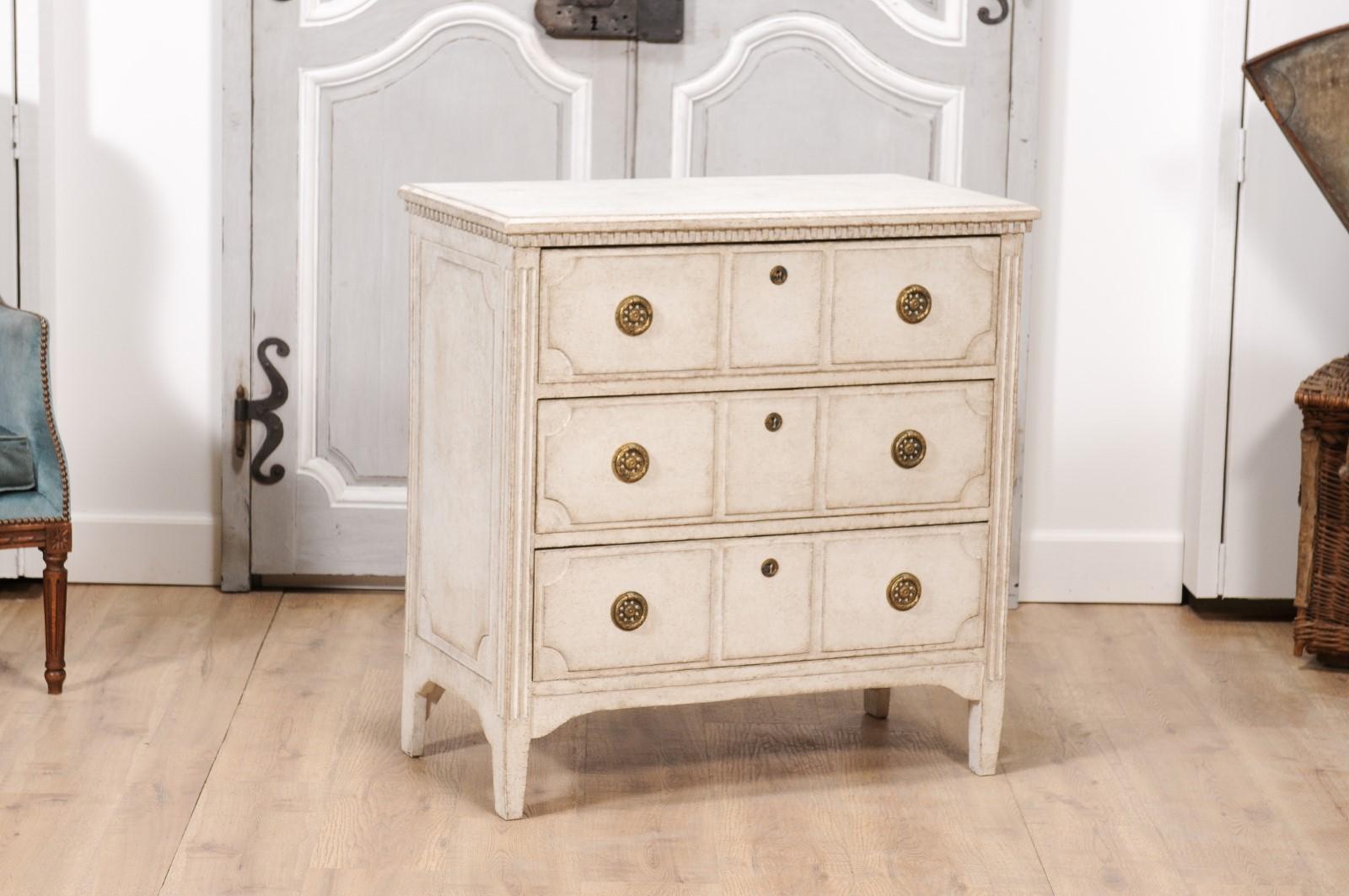 A Scandinavian Neoclassical style painted chest from the 19th century with three drawers, carved décor and brass hardware. This 19th-century Scandinavian Neoclassical style painted chest exudes understated elegance, harmoniously blending
