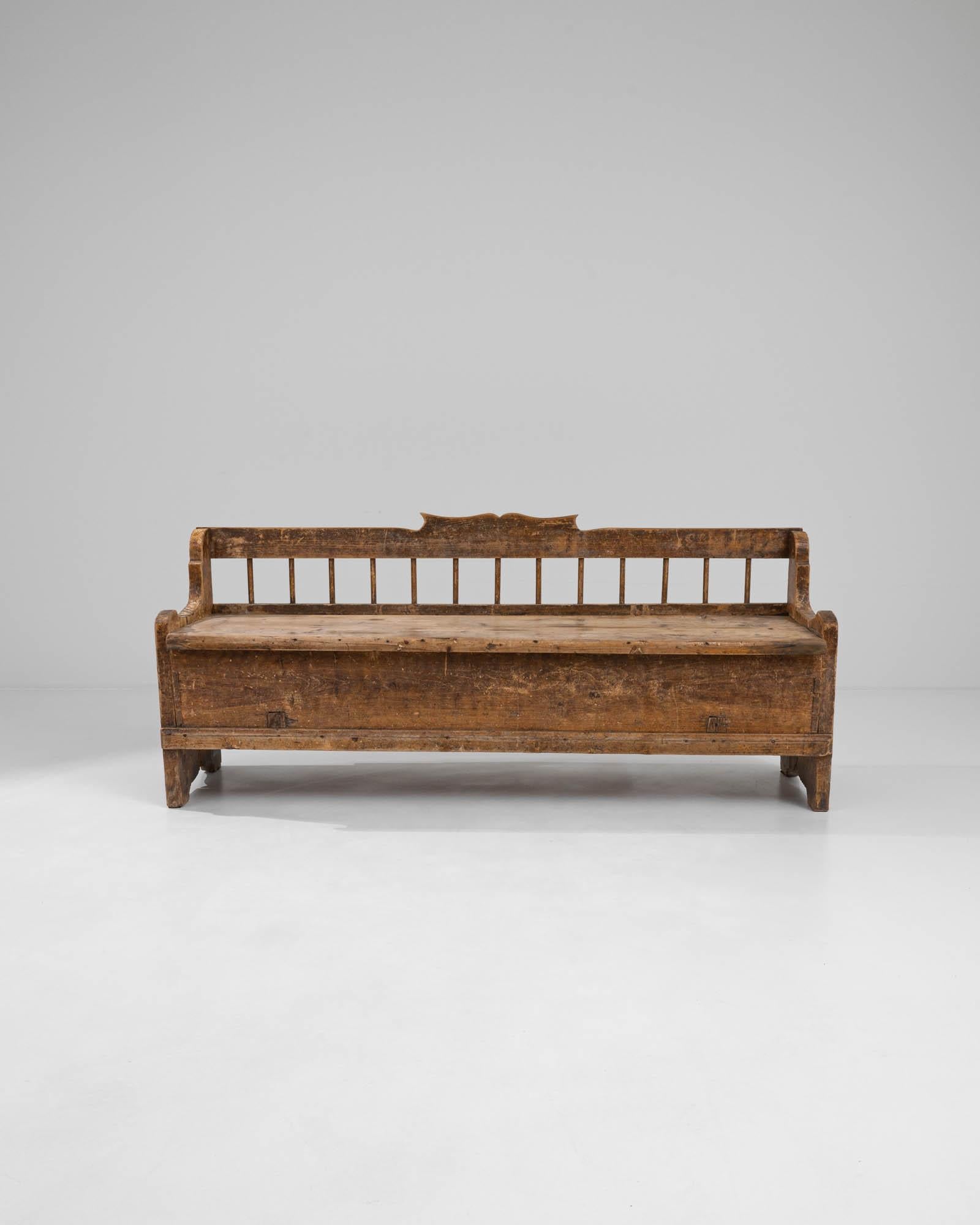 A wooden bench created in 19th century Scandinavia. Weathered, yet resiliently and timelessly elegant, this solid wood bench holds a mature poise. With thoughtfully curved arms, a sculpted back, and minimal backrest spindles, this artisanal bench