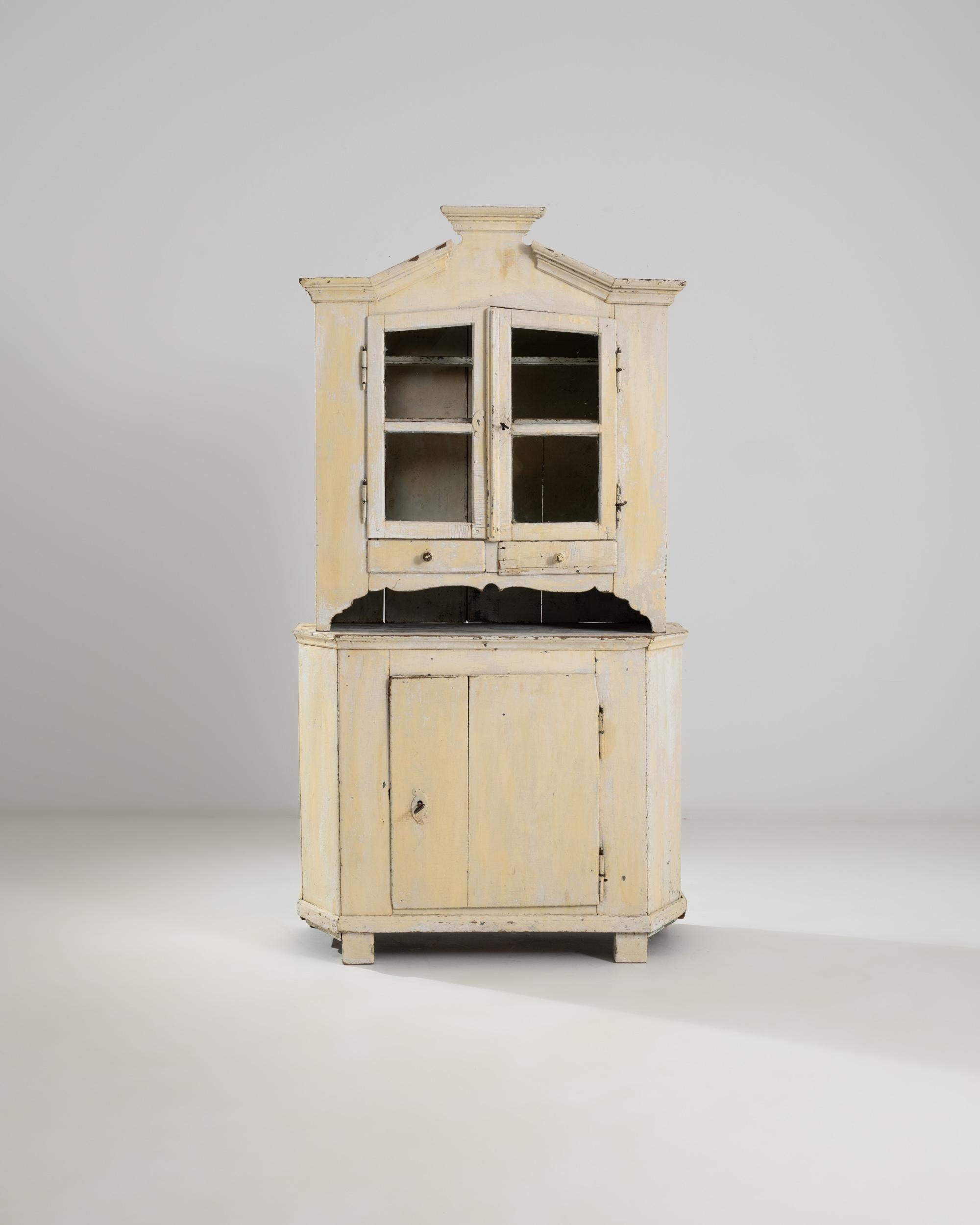 With a warm, butter-yellow patina and a rustic silhouette, this antique Scandinavian farmhouse vitrine radiates a wholesome charm. Built in in the 19th Century, the peaked crown of the cabinet evokes the pointed roofs of traditional Scandinavian