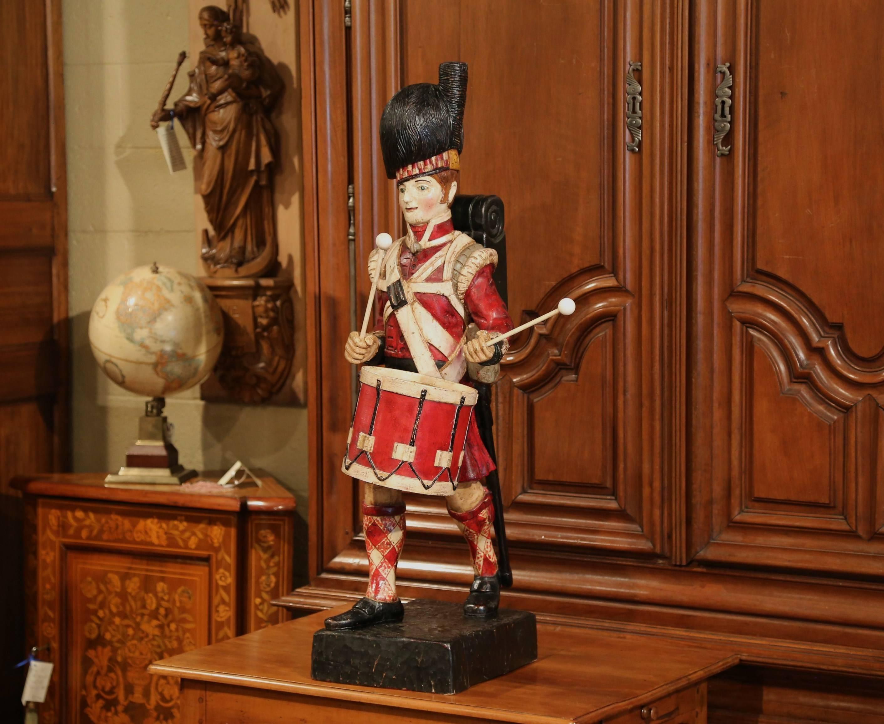 This beautiful, antique wood figure was crafted in Scotland, circa 1890. The large carving features a traditional Scottish military drummer with carved hat, backpack, sword, drum and drumsticks. Standing on a square base, he is wearing a red coat