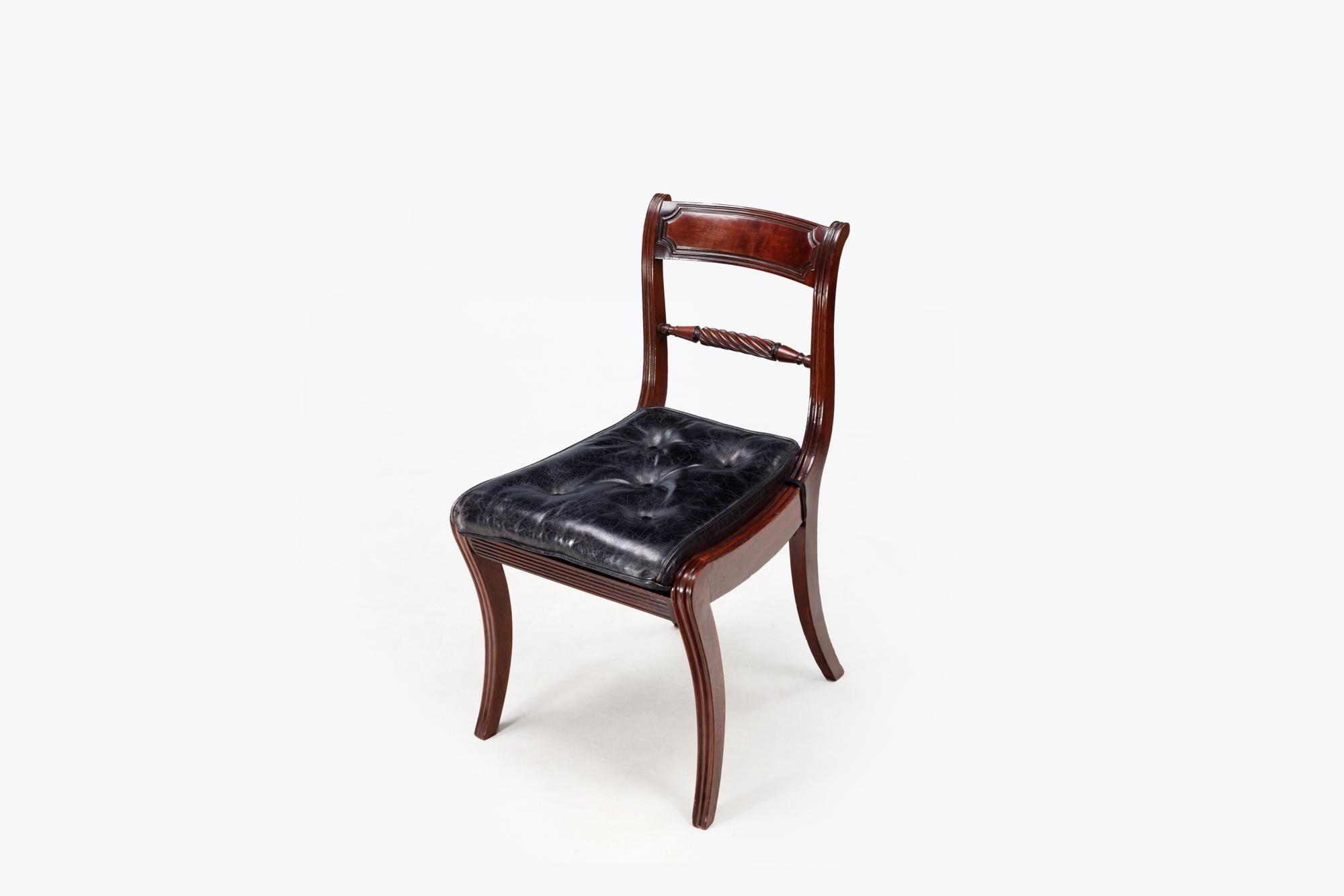 Set di diciotto sedie da pranzo Regency in mogano con gambe a sciabola e sedute in pelle nera con bottoni. Gli schienali a pannelli reed sovrastano una spalliera centrale in corda, e tutte le sedie sono dotate di sedili bergère, rivestiti di cuscini