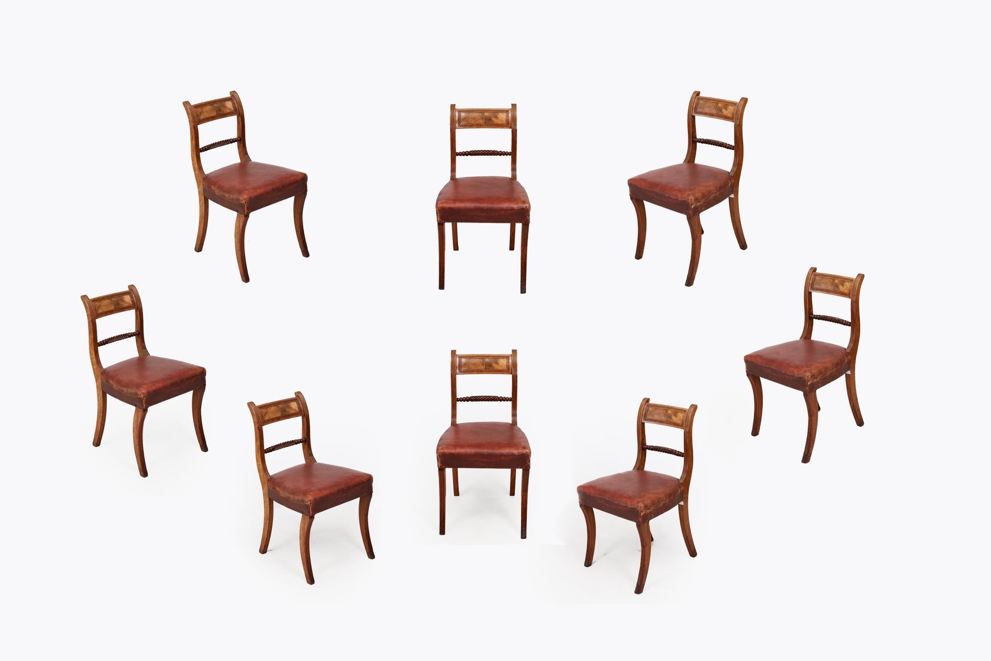 19th Century set of eight Regency period dining chairs in light mahogany with enclosed bar backs and ropetwist centre rails. The seats are covered in leather, which has a well aged patina, and all eight sit on sabre legs to the front and rear.