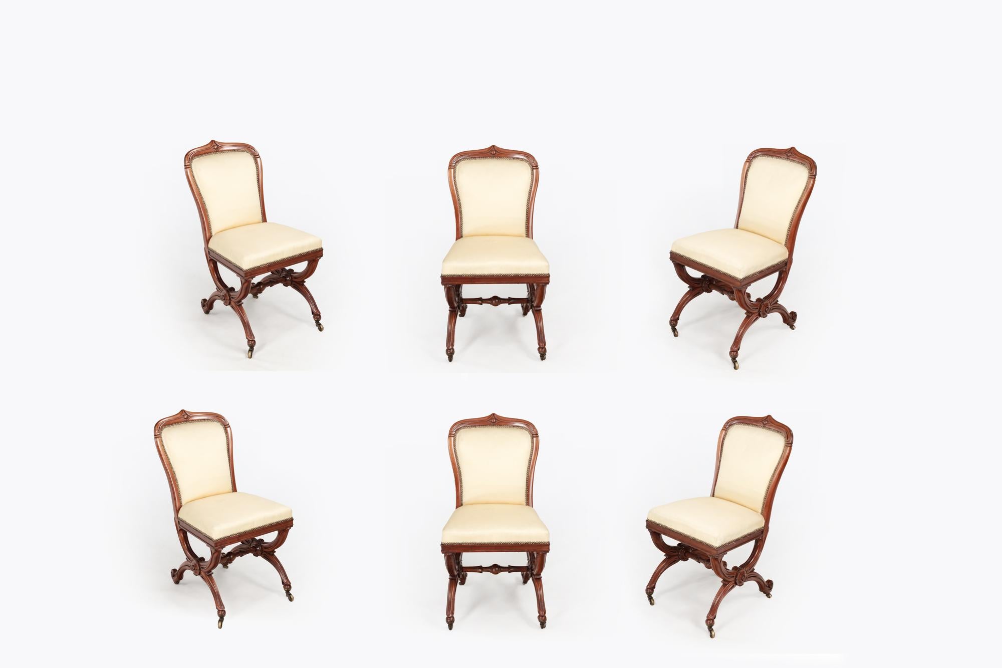 19th Century set of six dining chairs with X-shaped mahogany frames and padded backs. Central carved rose detail to the X-frame legs joined by a molded spacers terminating with scolled feet on simple brass castors. Stamped with the mark 