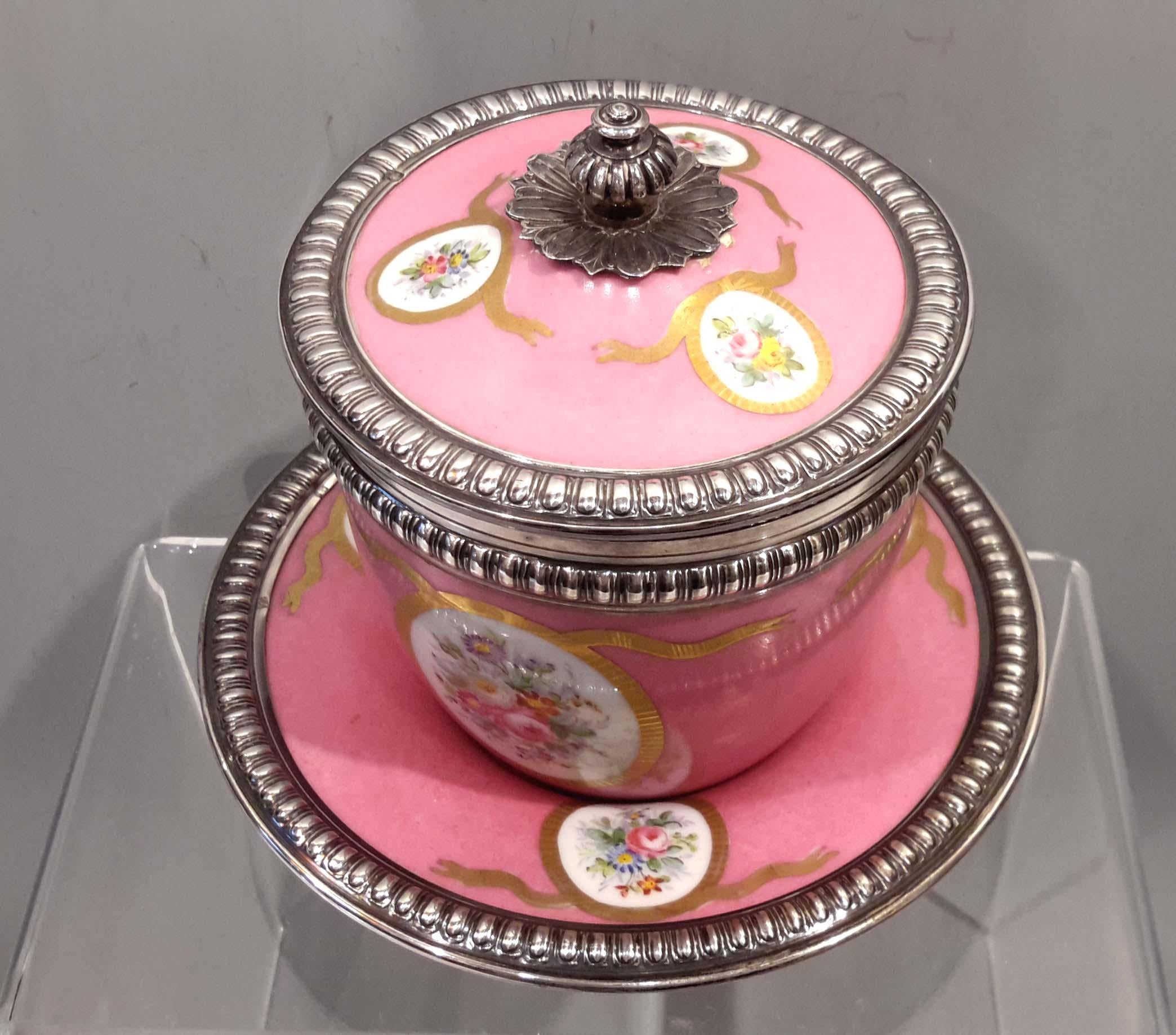 A late 19th century French Sèvres porcelain lidded cup and saucer in pink with floral cartouches and sterling silver mounts. The sterling rims are hallmarked 950 silver with the hallmark of Henri Lapeyre.