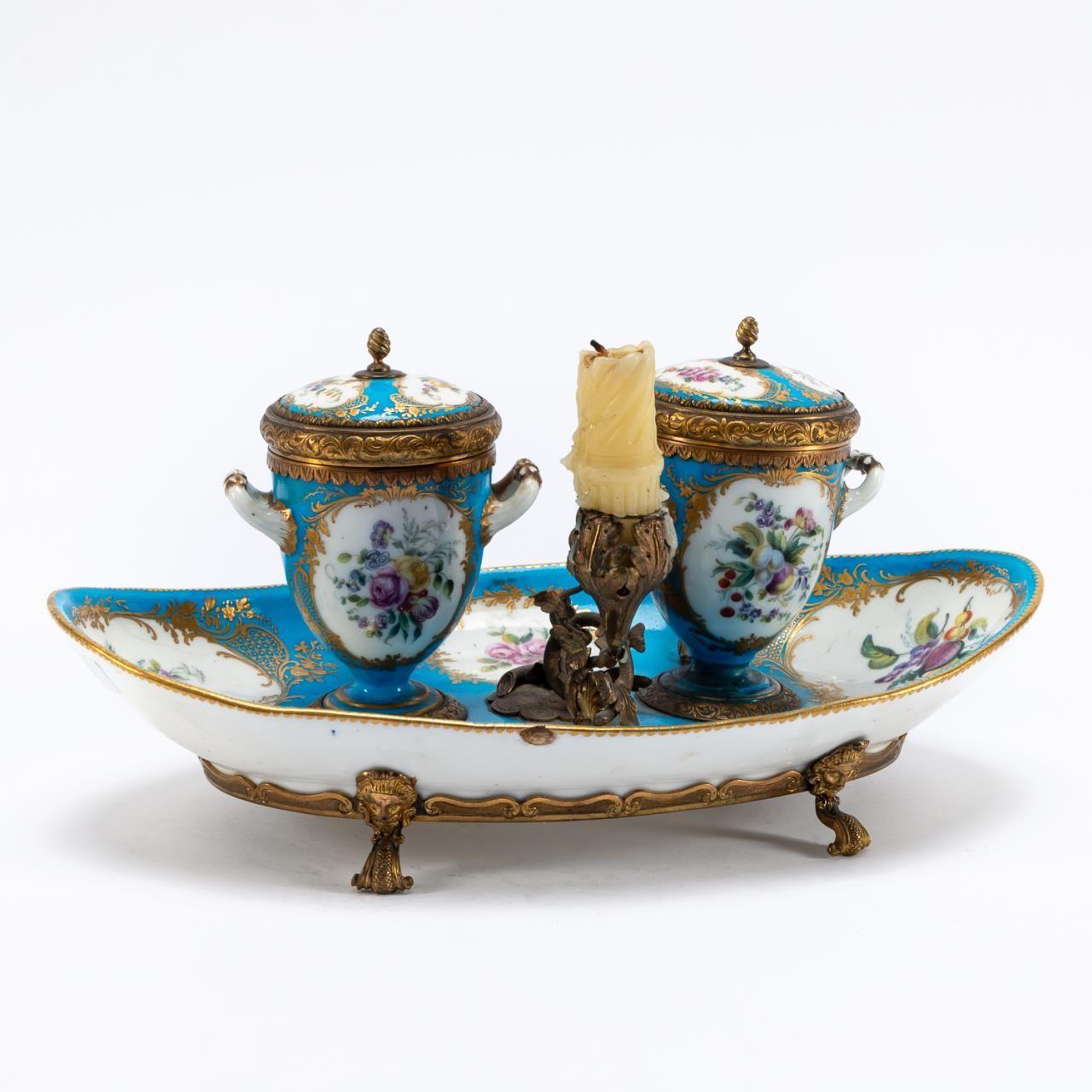 French, 19th century. Bronze ormolu mounted blue ground porcelain navette- form footed encrier or inkstand in the manner of Sevres, having gilt accented reserves decorated with florals, two inkwells with glass liners, single candleholder, and pen