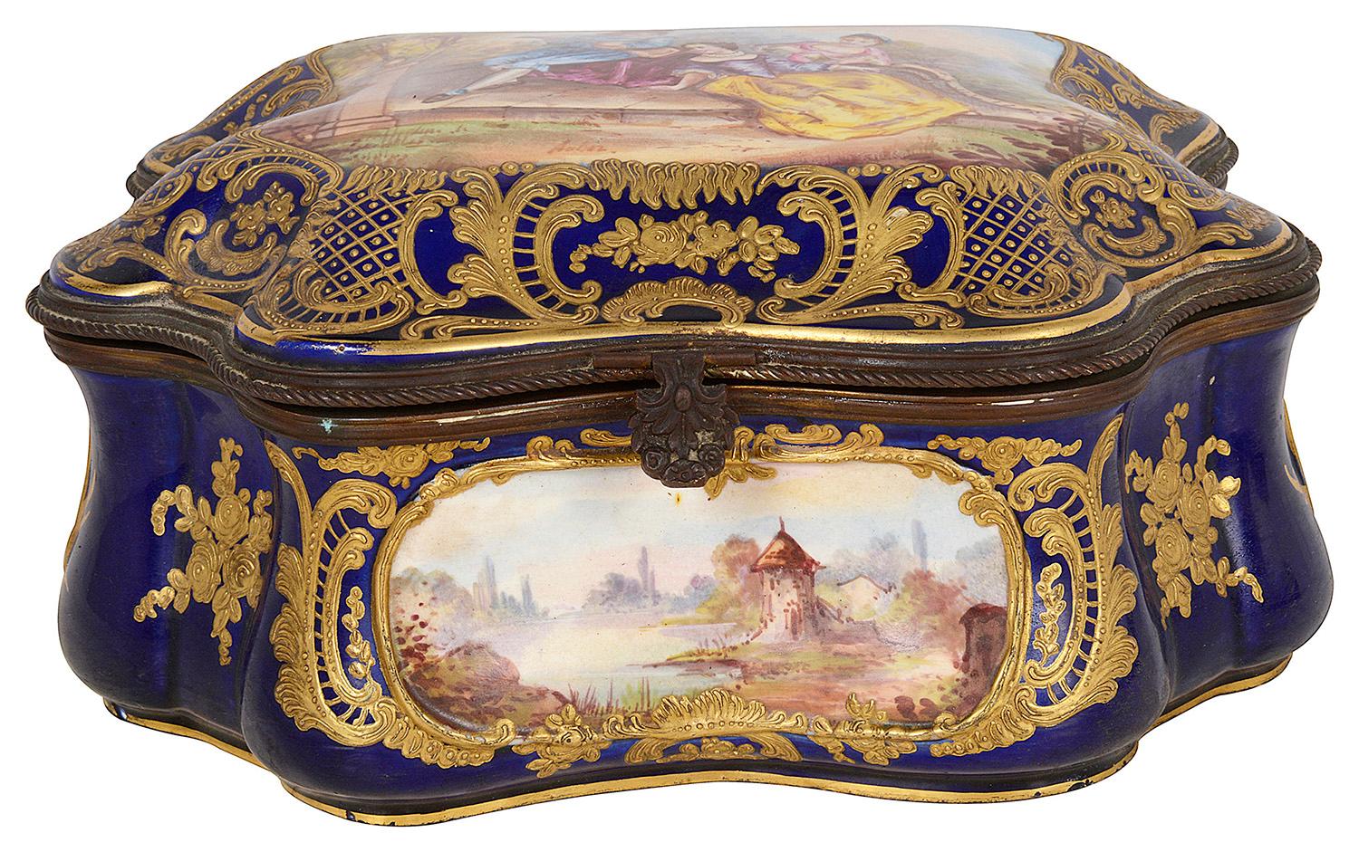 A very good quality late 19th Century French Sevres style porcelain casket, having a Cobalt blue ground, scrolling and floral gilded decoration, inset hand painted lakeland scenes, a romantic scene to the lid of a musician serenading a young lady