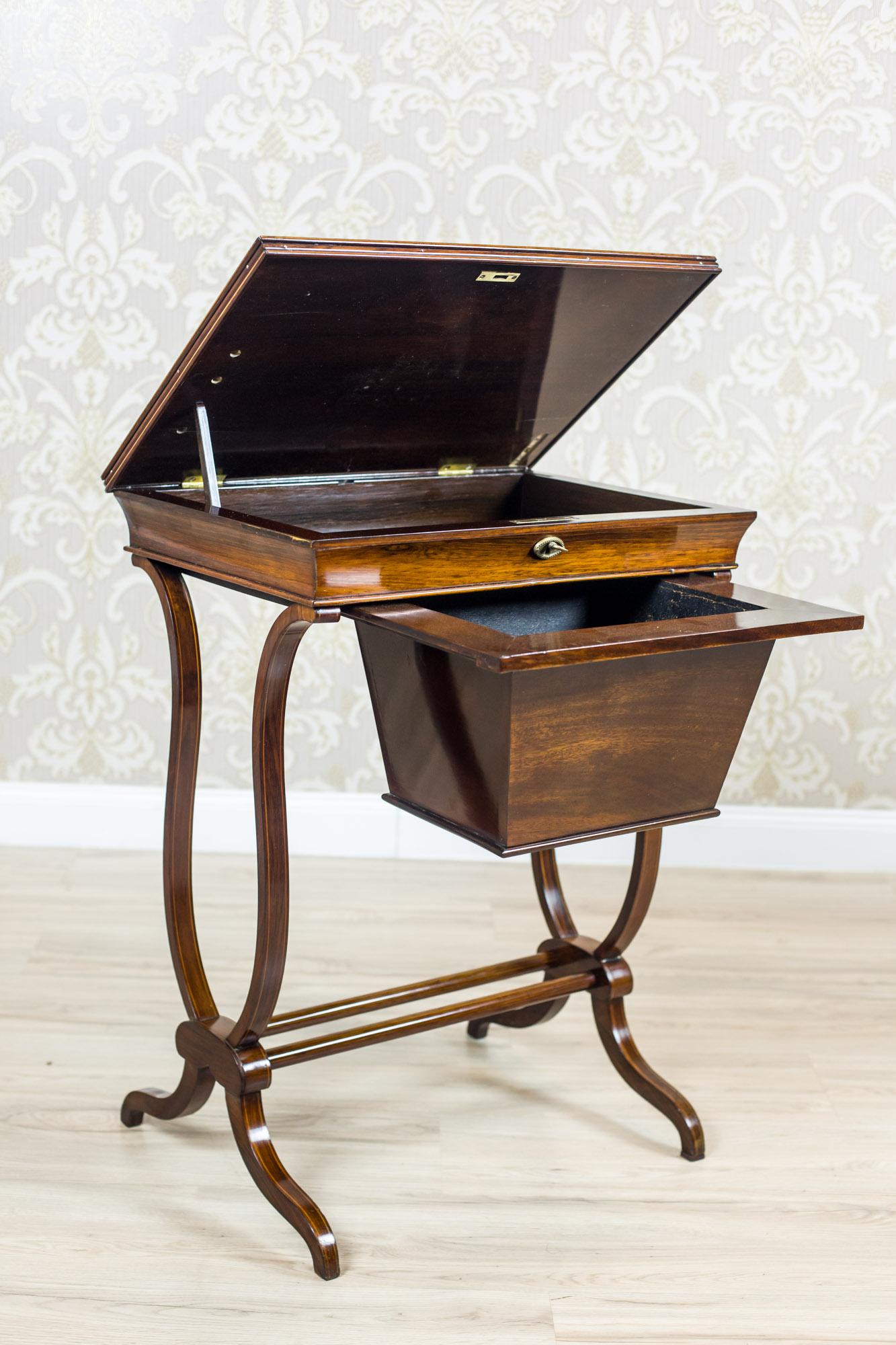 We present you this antique sewing table, circa 1820, made of rosewood.
The table is equipped with a shallow compartment under the liftable top and a basket for needlework in the form of a drawer suspended underneath.
The legs are in the shape of