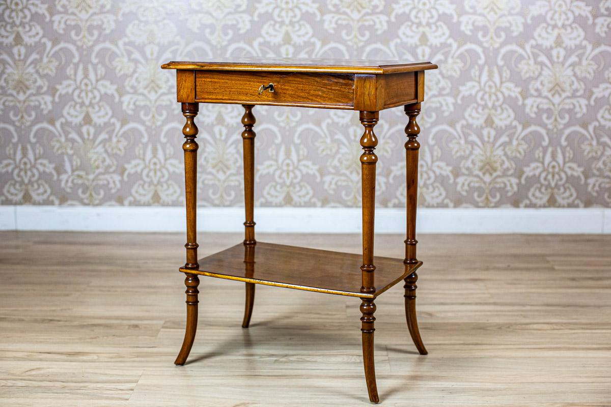 Table de couture du 19e siècle avec dessus marqueté

Nous vous présentons une table de couture de la fin du 19e siècle.
Ce meuble est composé d'un tablier rectangulaire qui s'ouvre vers le haut et est posé sur quatre pieds tournés.
Au lieu d'un
