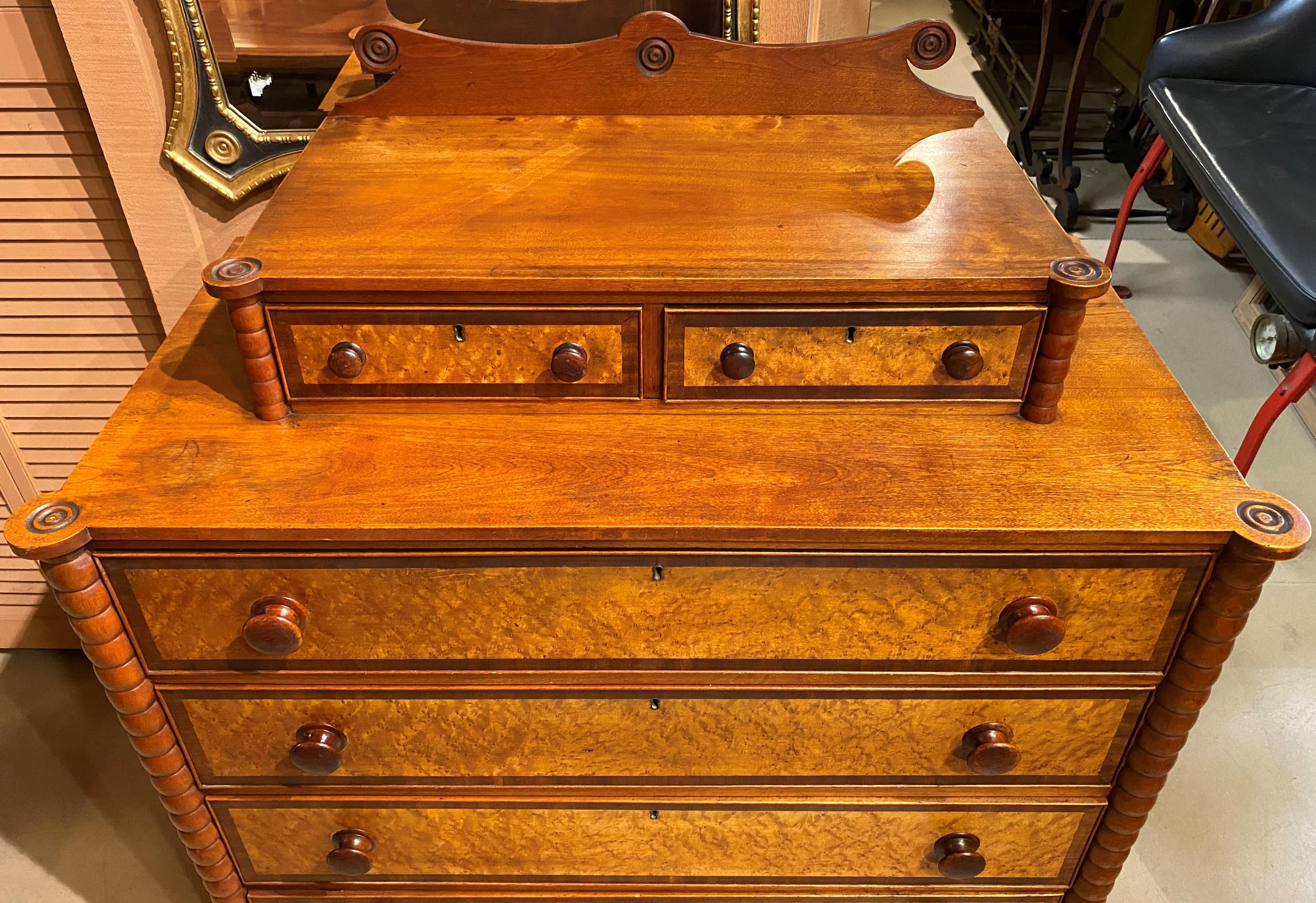 A fine 19th century Sheraton chest with a carved crest featuring bullseye decoration, surmounting two glove boxes over a case with turreted corners, four graduated drawers with bird's eye maple veneer drawer fronts with mahogany veneer borders,