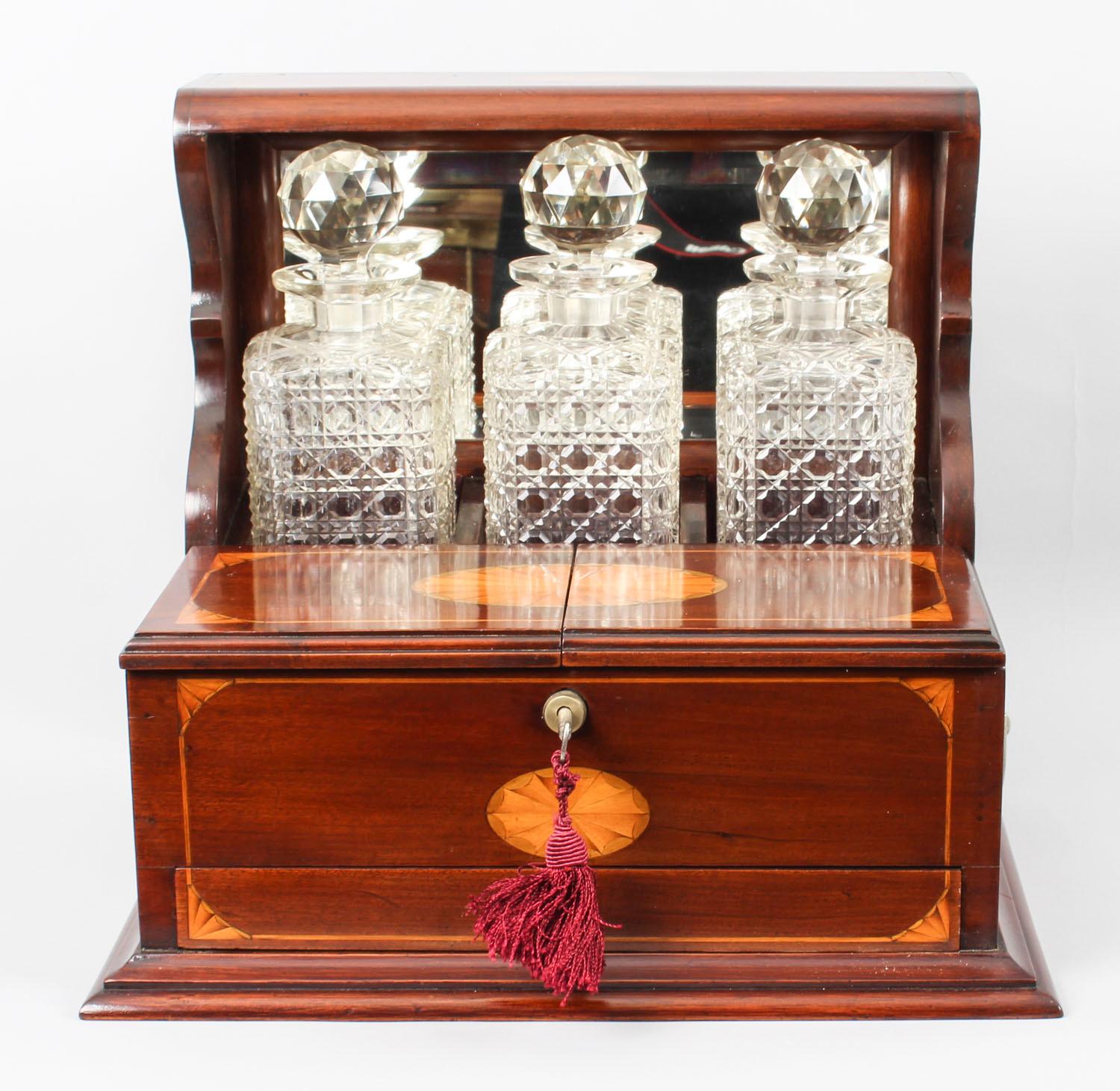 This is a superb antique Victorian mahogany cased three decanter Tantalus with decorative inlaid decoration, circa 1870 in date.

It was skillfully crafted in mahogany with beautiful shell and line inlaid decoration and stylish silver plated
