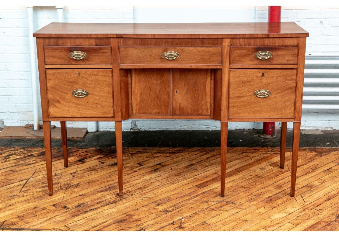 With a tall top and apron with two short drawers flanking a long drawer. The burled cabinet below with a deep drawer on the left side, the right side deep drawer with bottle storage compartments. With hammered oval brass pulls  and key escutcheons 