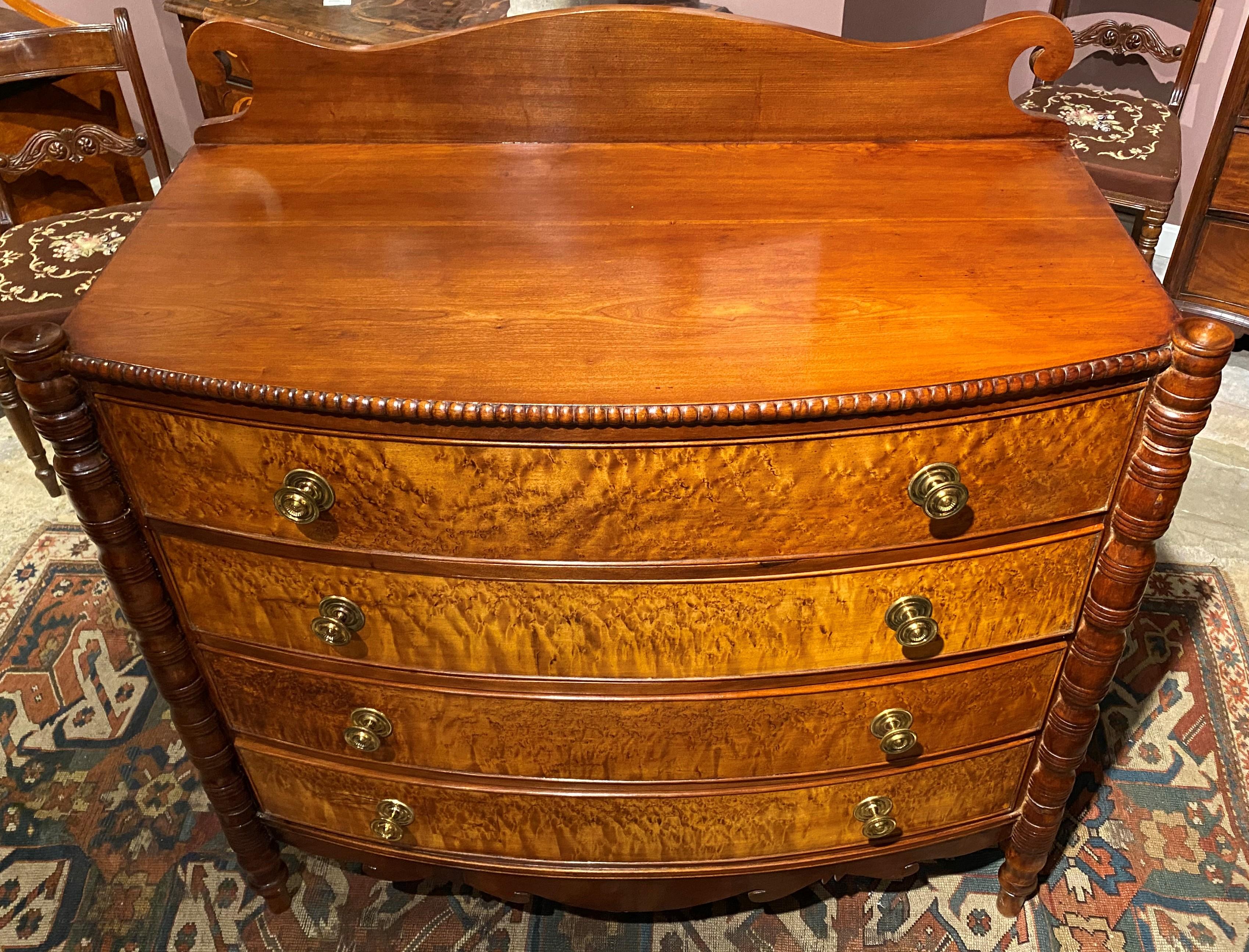 A beautiful Sheraton cherrywood swell front four-drawer chest with bird's-eye maple drawer fronts, a scroll-carved backsplash, gadrooned top edge on front and sides, turret front corners surmounting turned columns, and scroll shaped skirt, all