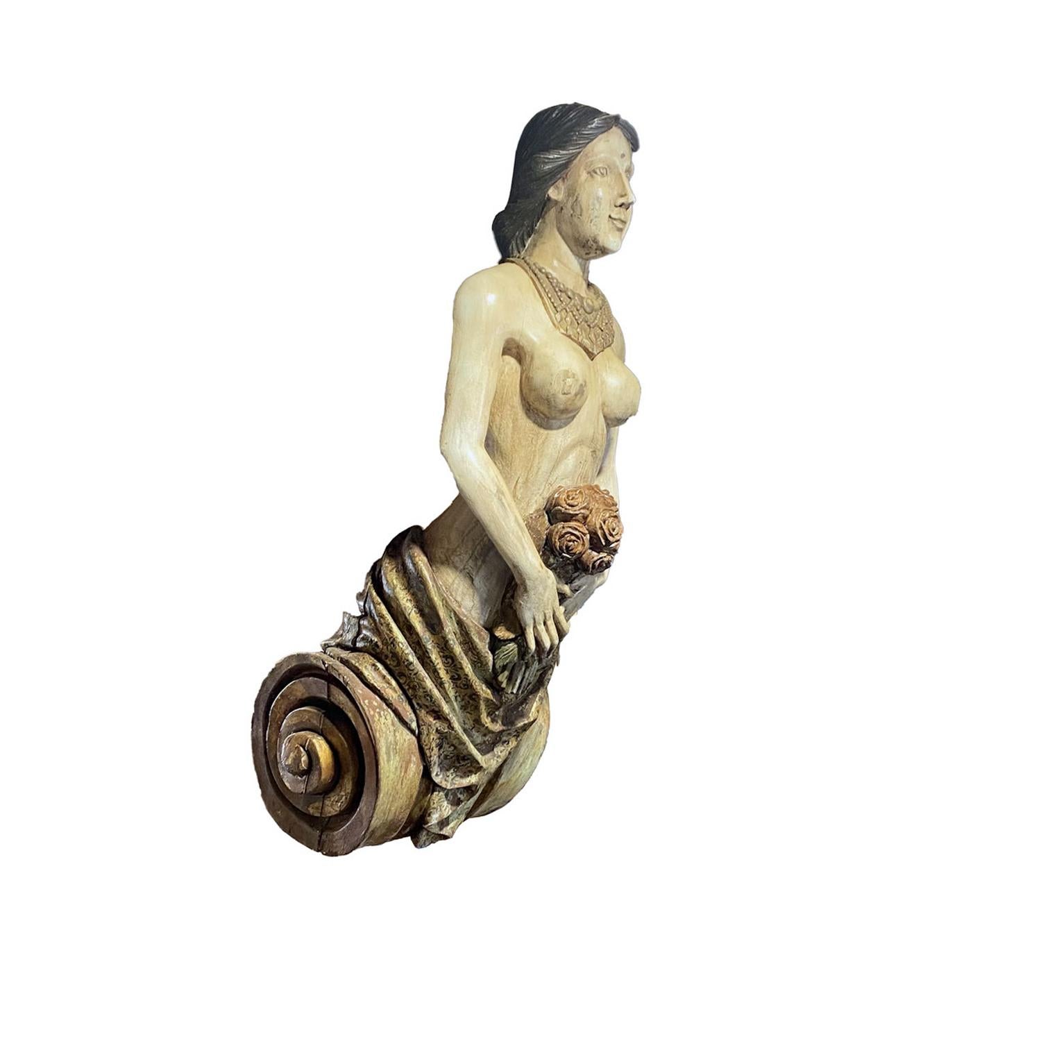 Carved ship figurehead of a woman wearing an elaborate gold necklace and holding a bouquet of roses at her waist. The lower part of her body is wrapped in a furled that is gilded and painted and rises from a scroll carved base, English, late 19th