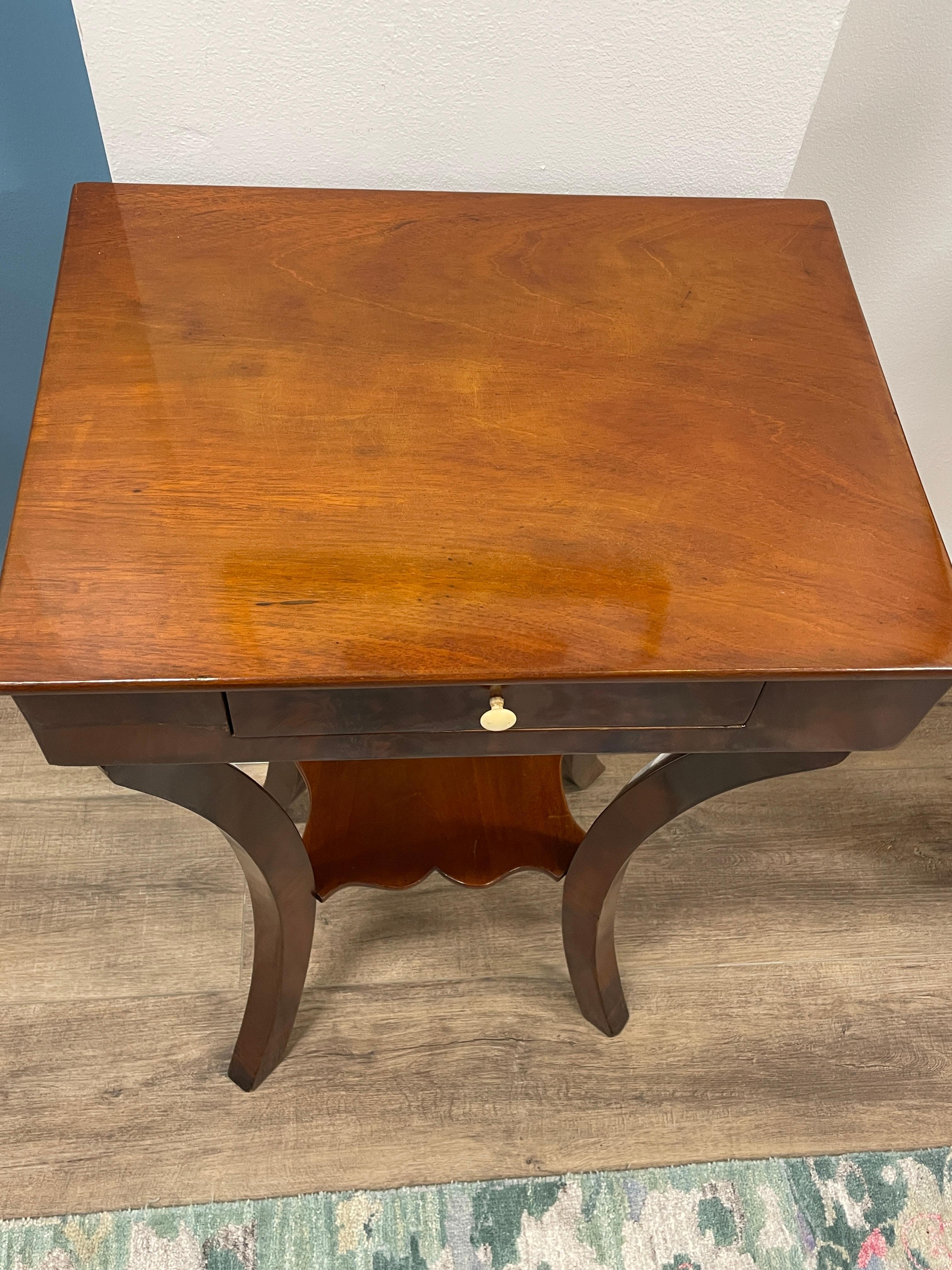 Discover a Biedermeier side table adorned with graceful curved legs, showcasing timeless elegance. This charming piece boasts a single central drawer complete with its original knob, adding a touch of authenticity. Crafted with a mahogany veneer,
