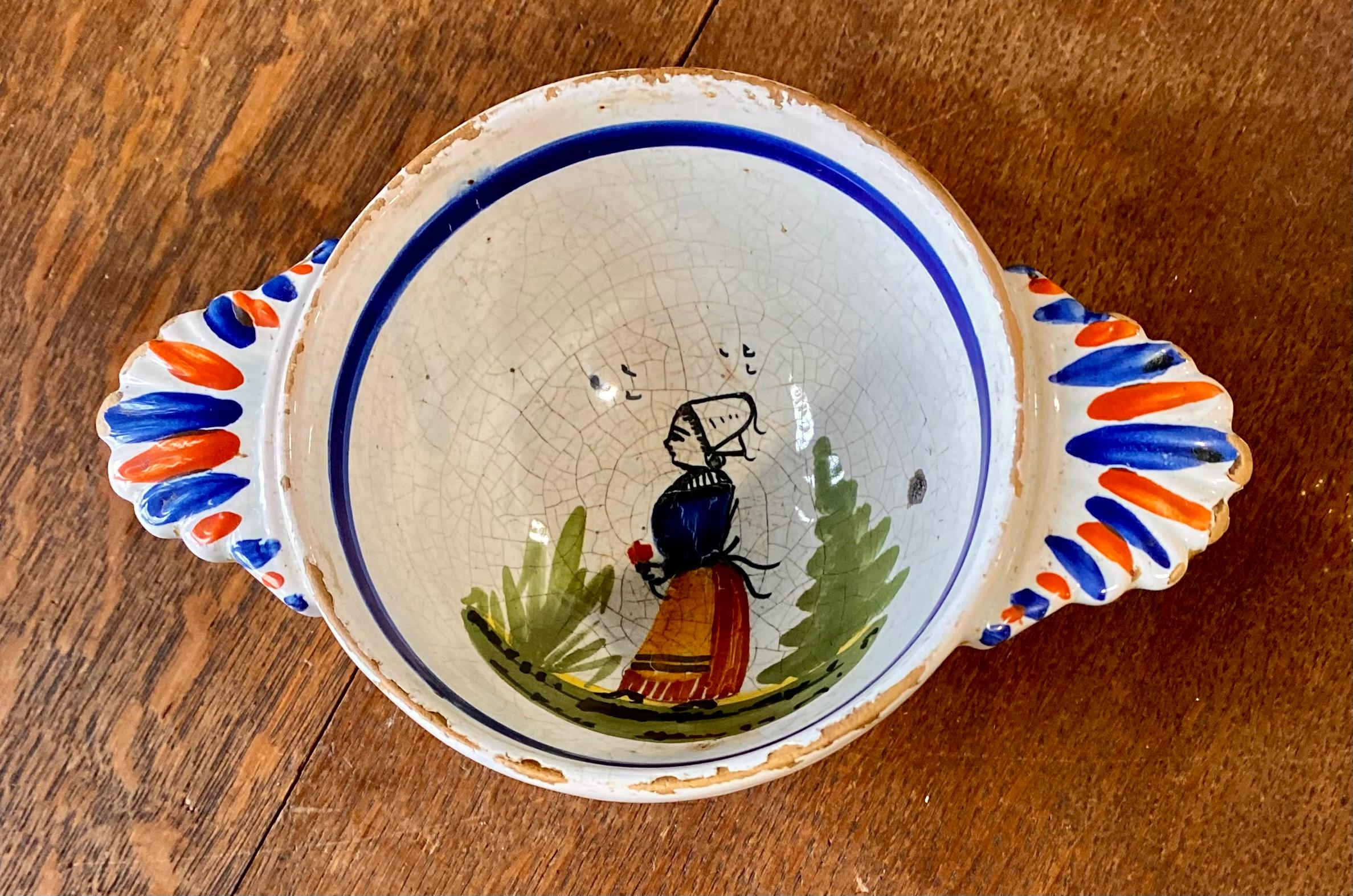 A beautiful old Quimper bowl signed HB Quimper. It is hand painted with the image of a Breton woman in traditional costume walking through a forest, featuring tree and flower motifs. This piece dates to the late 1800s. There is a slight rubbing on
