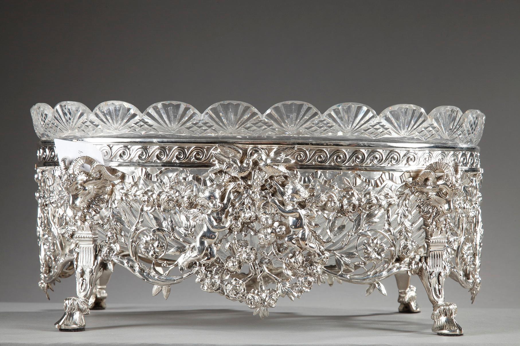 Silver jardinière composed of a cut-crystal, oval bowl resting in a silver frame. The scalloped edge of the crystal bowl is decorated with radiating and diamond-shaped patterns. The silver frame is richly decorated with openwork ribbons, Greek