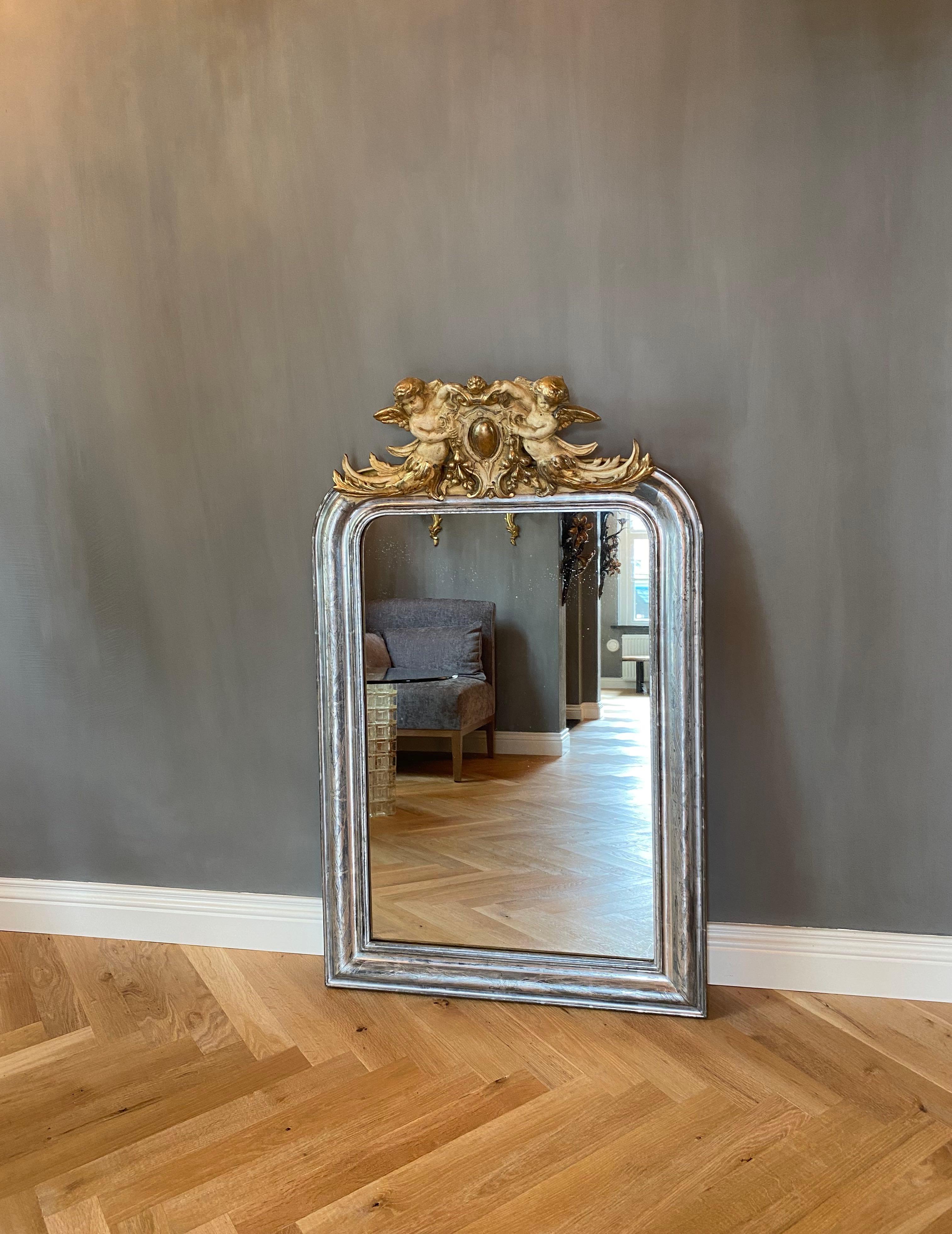 Very pretty 19th c. French mirror with its original slightly foxed antique glass and silver leaf gilding.
The beautiful open work crest is representing two cherubs or putti holding a central medalion.
The frame is etched with flowers and leaves.
The