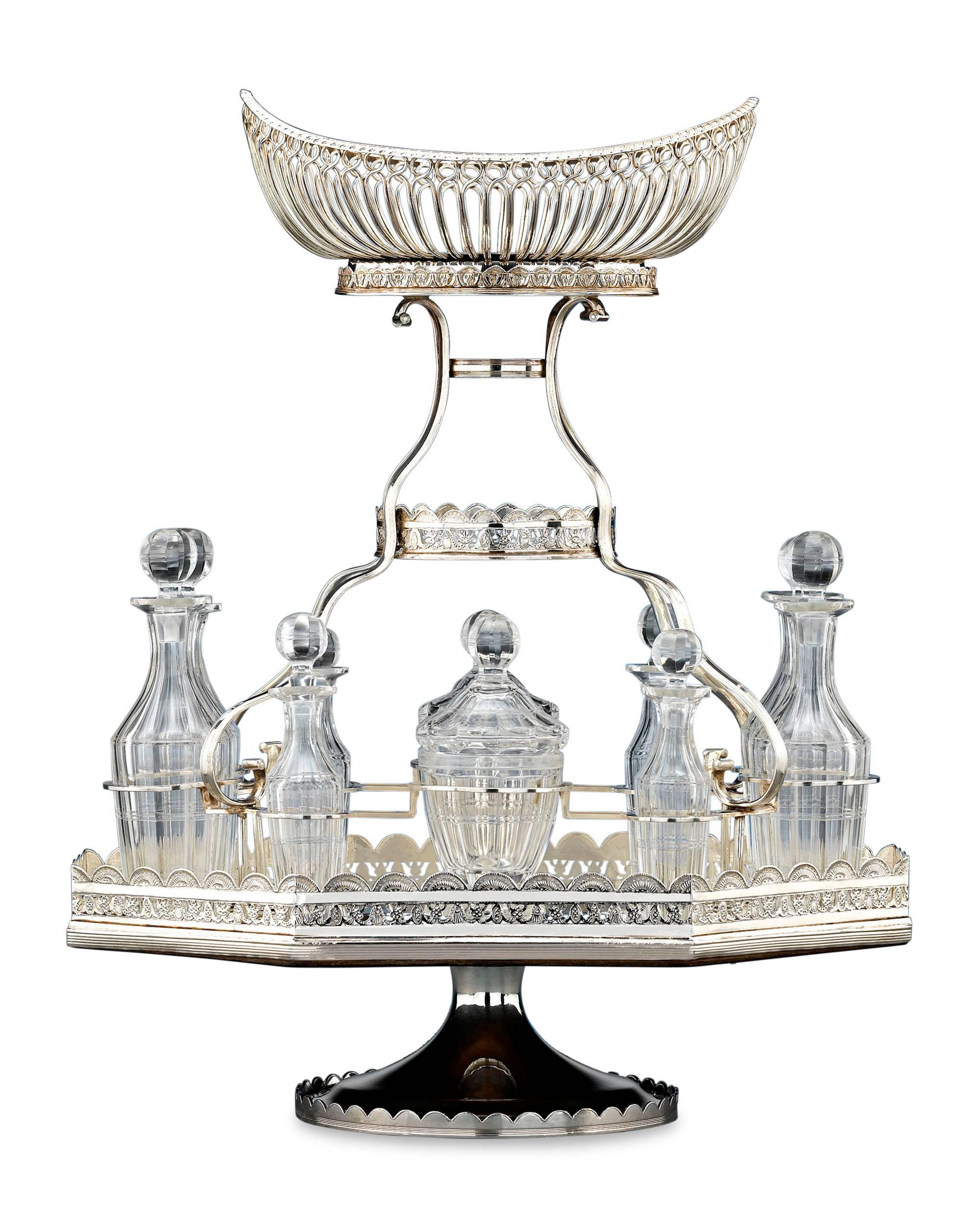This elegant silver plate epergne is a rarity in that it also includes a full, cut-glass cruet set. This service’s delicate central basket is elevated above a plateau holding ten finely-cut bottles, including two mustard pots, four small