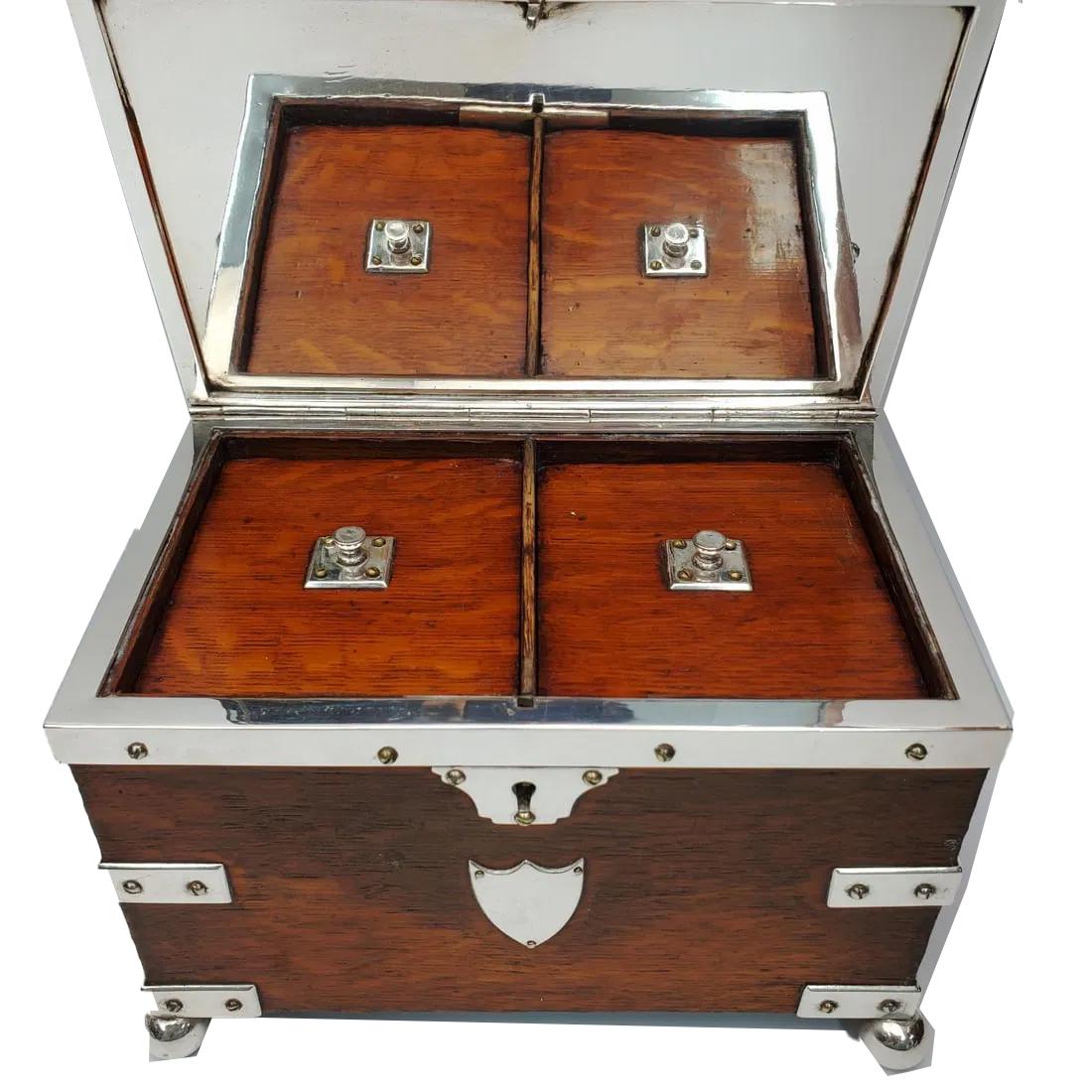 Caja de té de doble cámara, de roble, montada en bandeja de plata, del siglo XIX. El cuerpo rectangular con tirantes y asas laterales de chapa de plata, elevado sobre pies de bola y con una tapa grabada con bisagras que se abre a un par de tapas de