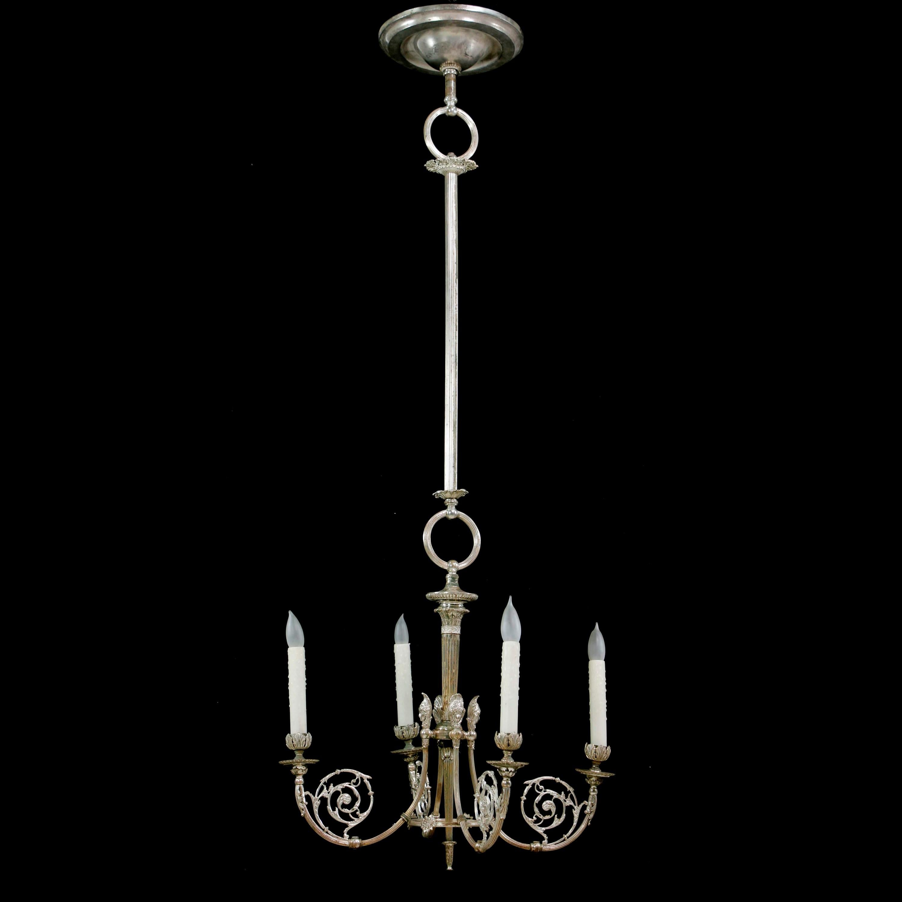 This lovely 19th century silver plated brass chandelier was originally a gas chandelier. It has fine filigree detail and features four women's heads. One at the base of each candelabra light. The silver shows natural wear with brass highlights