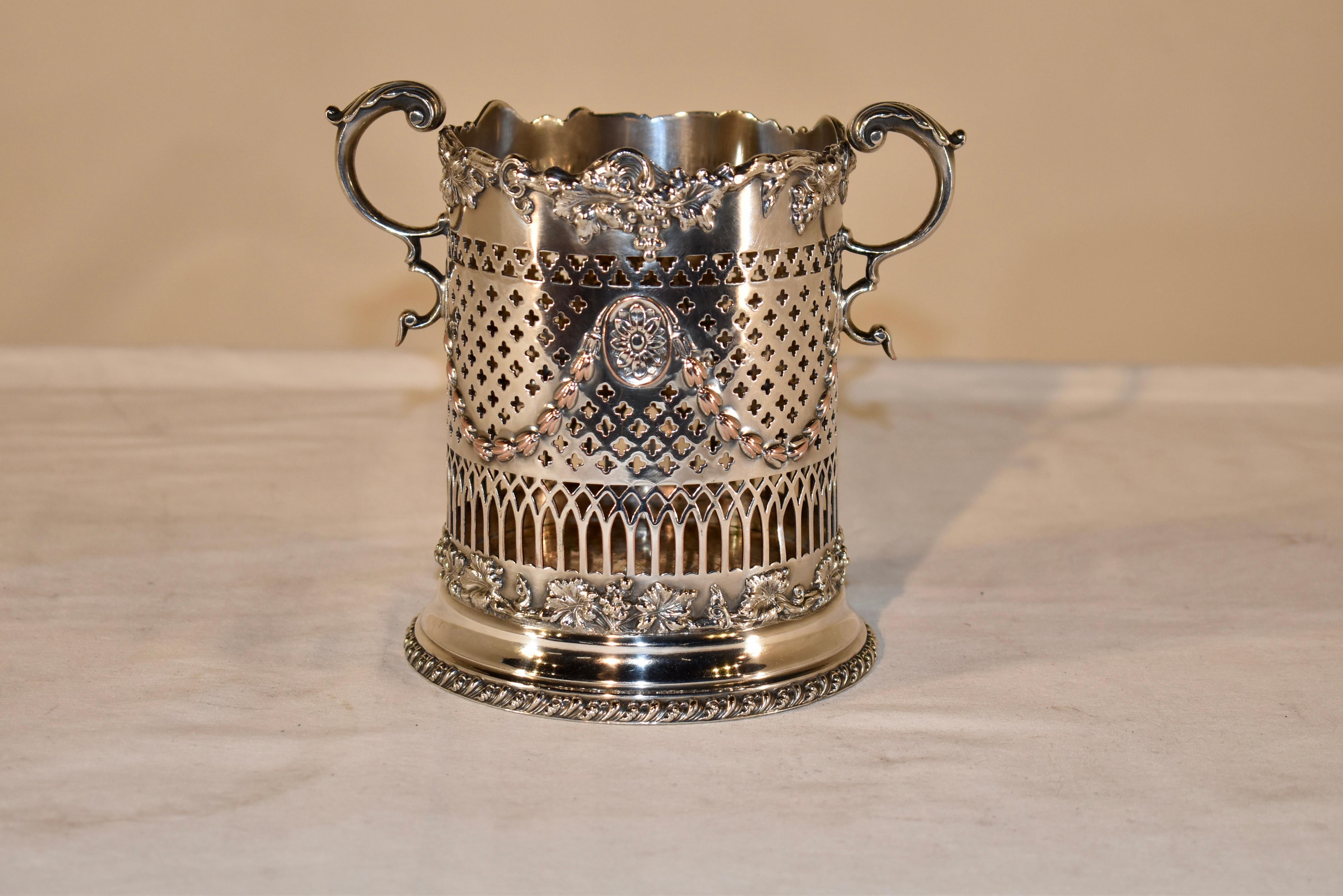 Late 19th century silver plated wine bottle holder from England.  This is a lovely form.  There are two handles, one on wither side, which have acanthus leaves at the top of the handle and curving gracefully to join the side of the bottle holder. 
