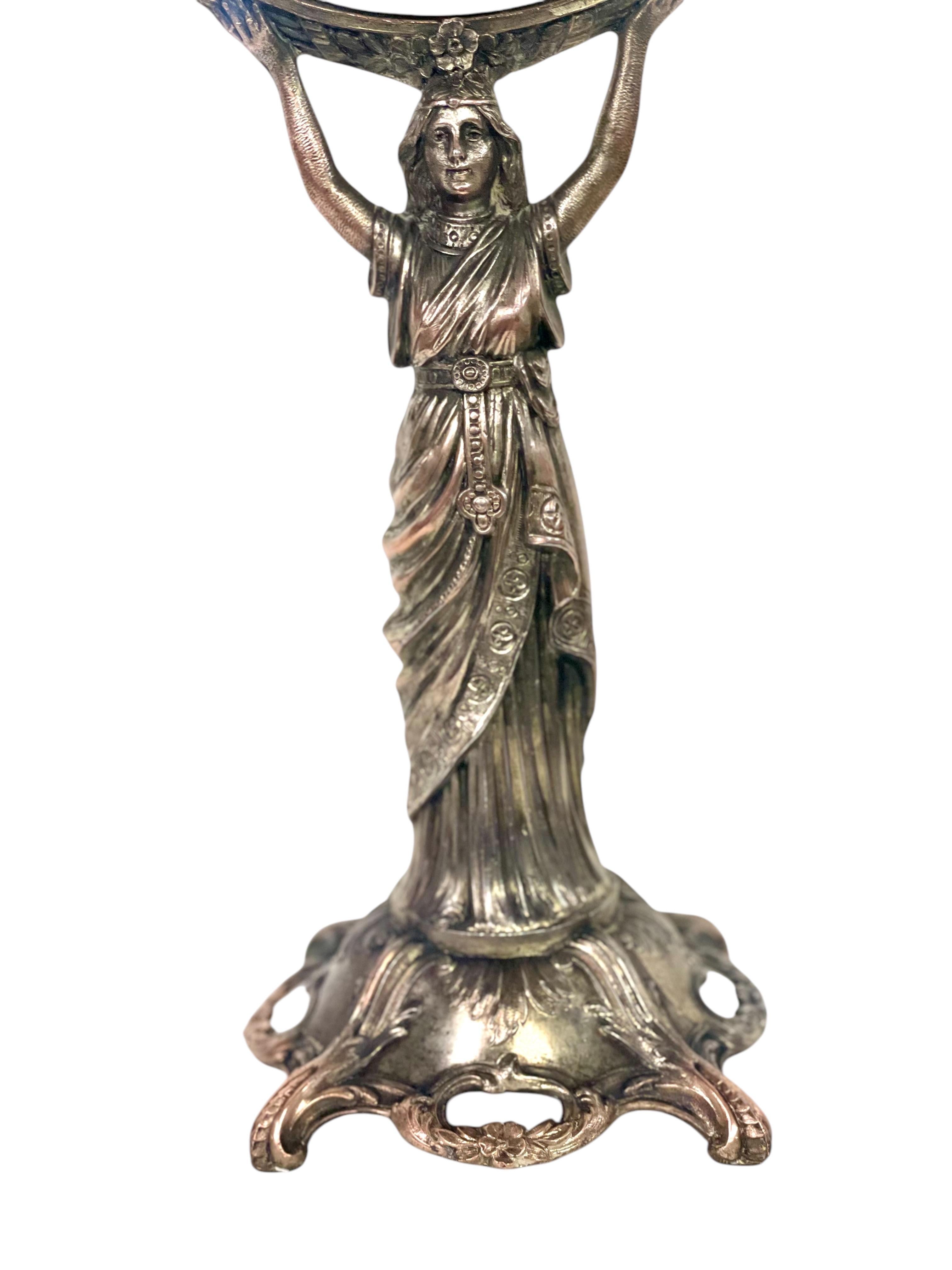 This elegant antique psyche mirror is a captivating example of late 19th century European craftsmanship. Cast in silvered bronze, the piece features a finely detailed draped female figure holding the mirror aloft in a classical pose, reminiscent of