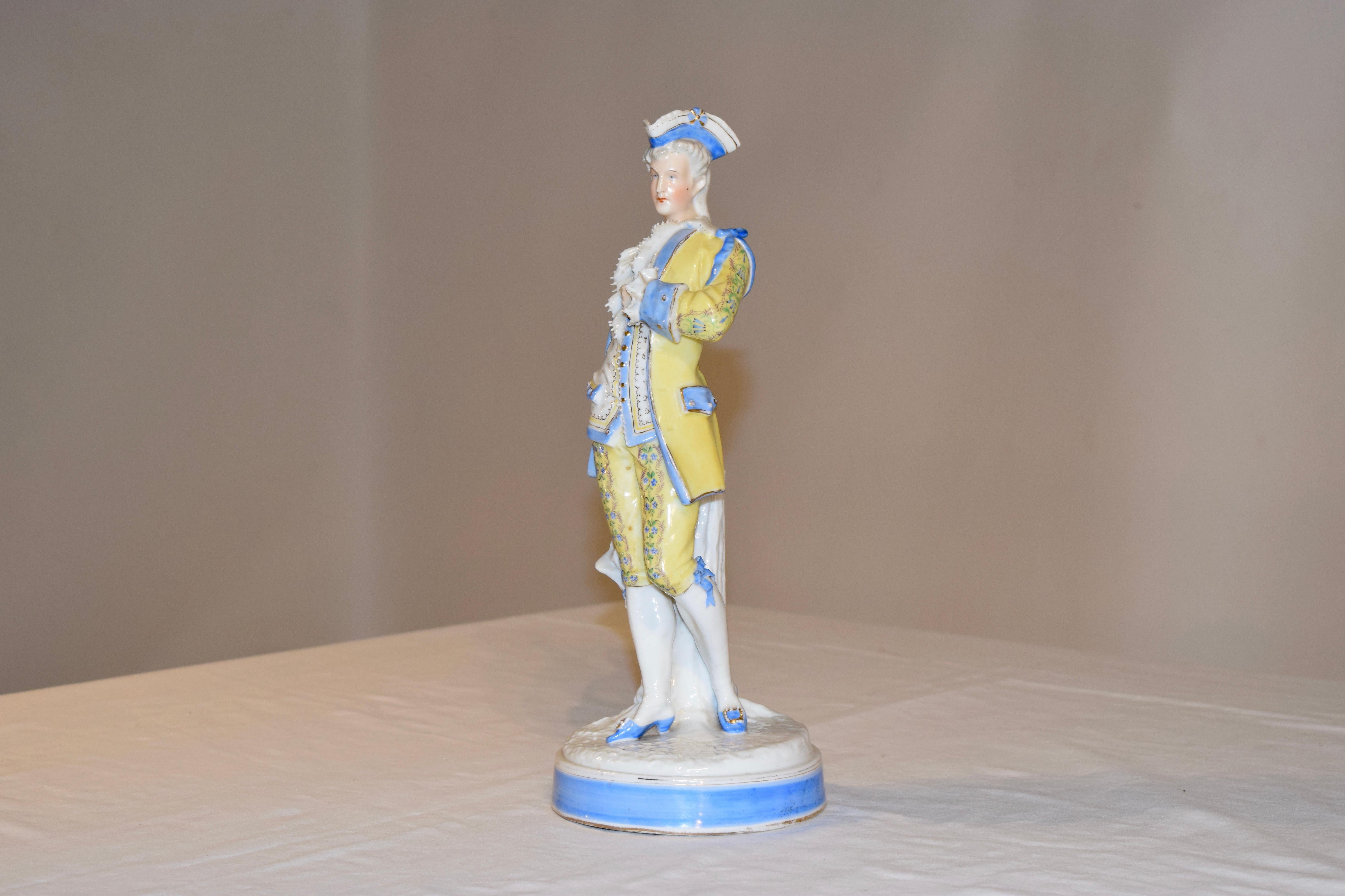 19th century Sitzendorf figure of a gentleman dressed in hand painted finery. He has a blue tricorn hat and a yellow suit, banded in lovely blue and hand decorated with florals and gold buttons. His shoes are blue as well with large buckle