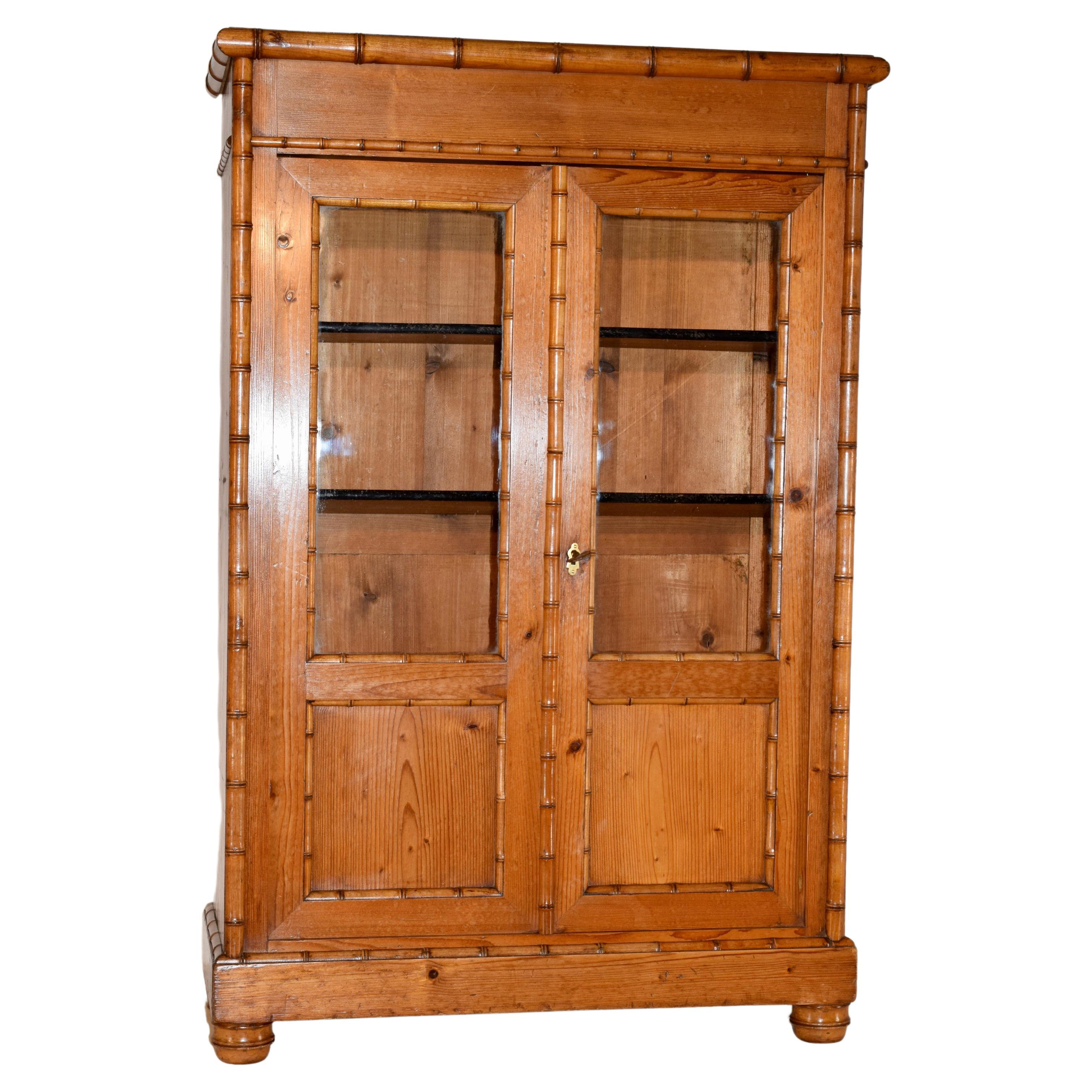 19th century small faux bamboo bookcase from France. The cabinet is made from pine and has hand turned bamboo style moldings made from cherry. The cabinet has two doors with glass panels, which open to reveal shelving. This is a great small bookcase