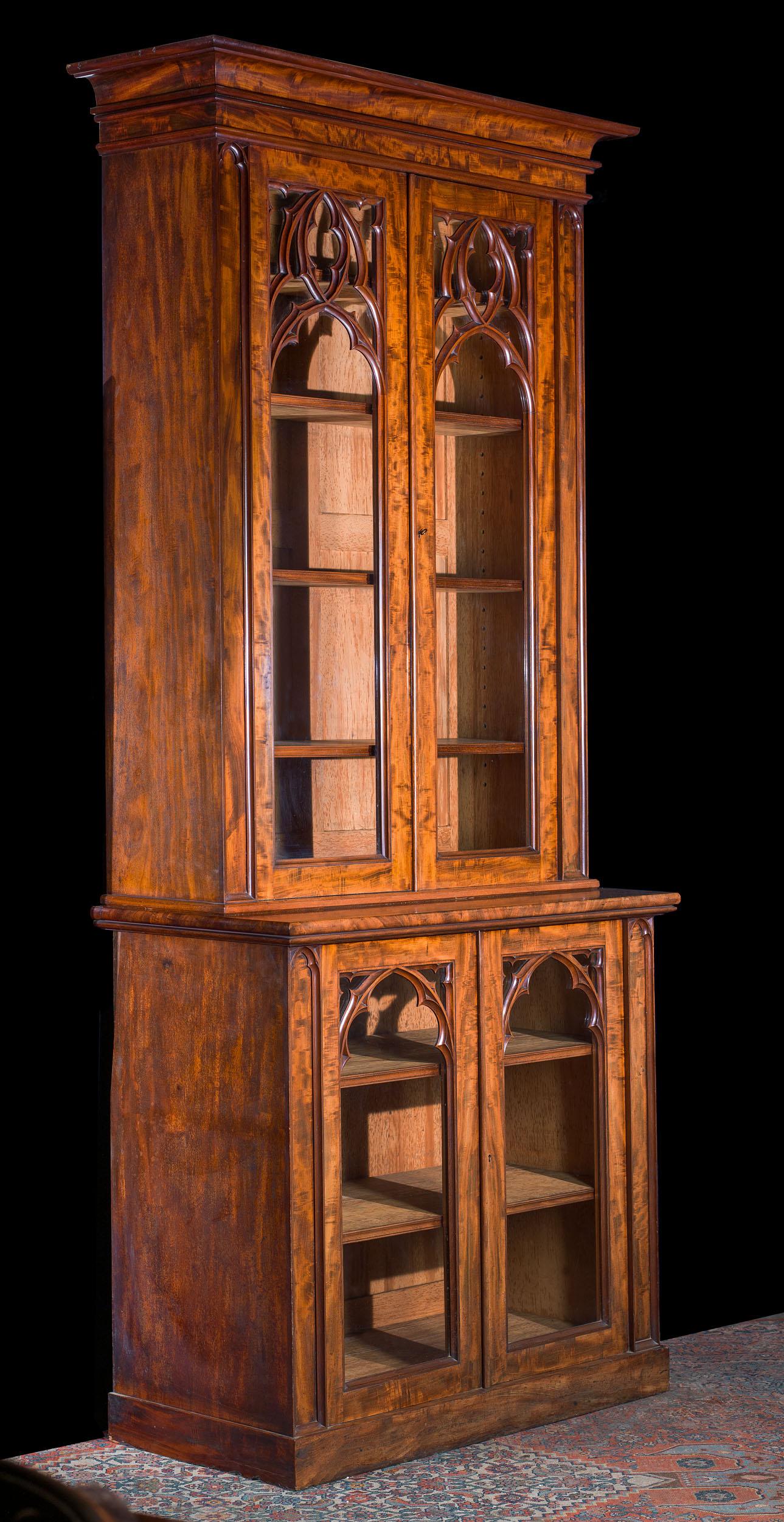 An elegant 19th century Gothic Revival glazed bookcase of small proportions and excellent quality. The figured mahogany case is mounted with two pairs of glazed doors, both carved with fine tracery reminiscent of Gothic windows. Inside the bookcase,