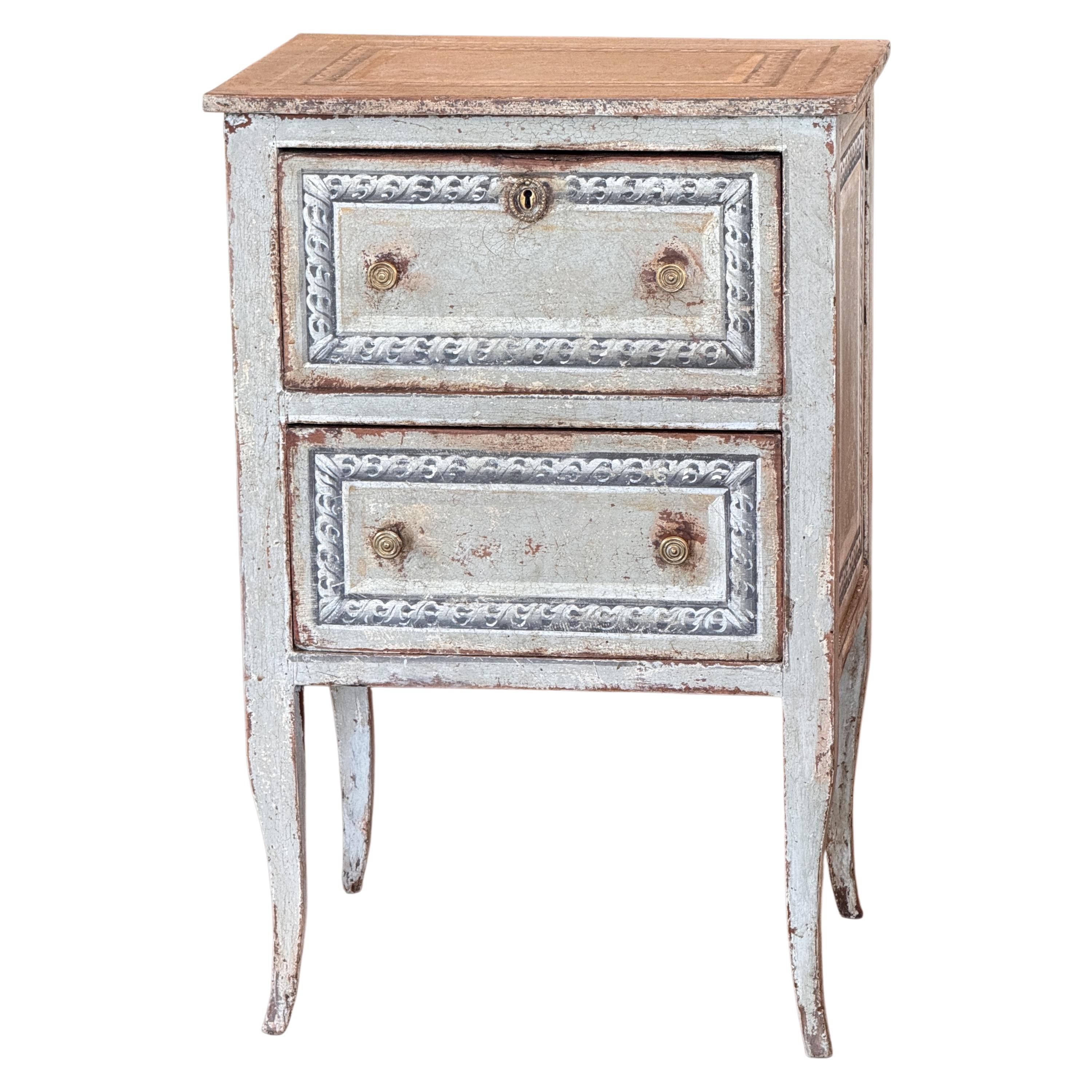 A charming 19th century Italian painted commode with two drawers and delicately carved details. The original painted surface shows an appealing aged patina, with soft blue-gray tones and contrasting molded panels. Raised on gently tapered legs, this
