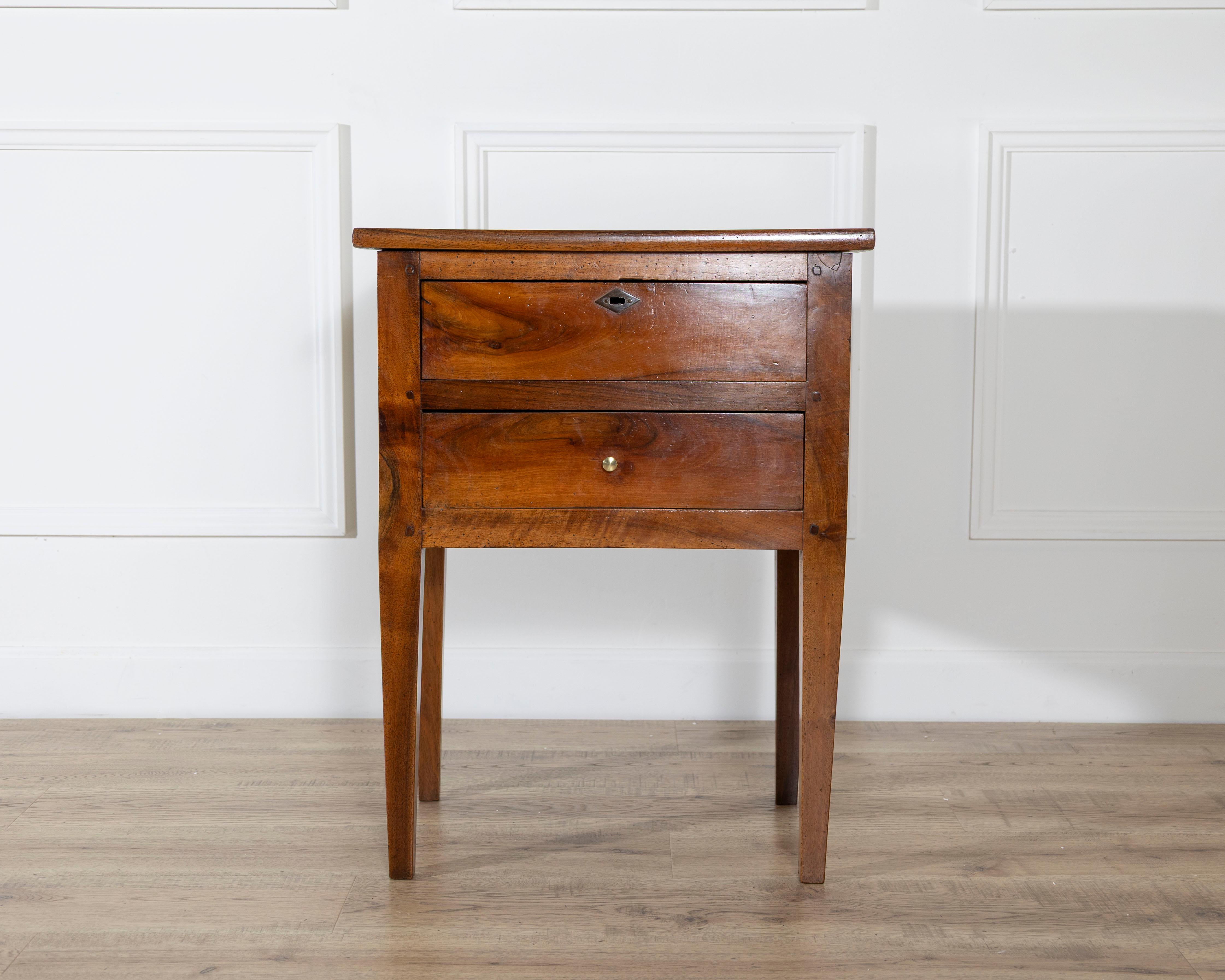 This small Louis XVI–style walnut chest features two front-opening drawers, the upper fitted with a functioning lock and key and the lower with a simple brass knob. The proportions are compact and slightly elevated, giving the piece an uncommon