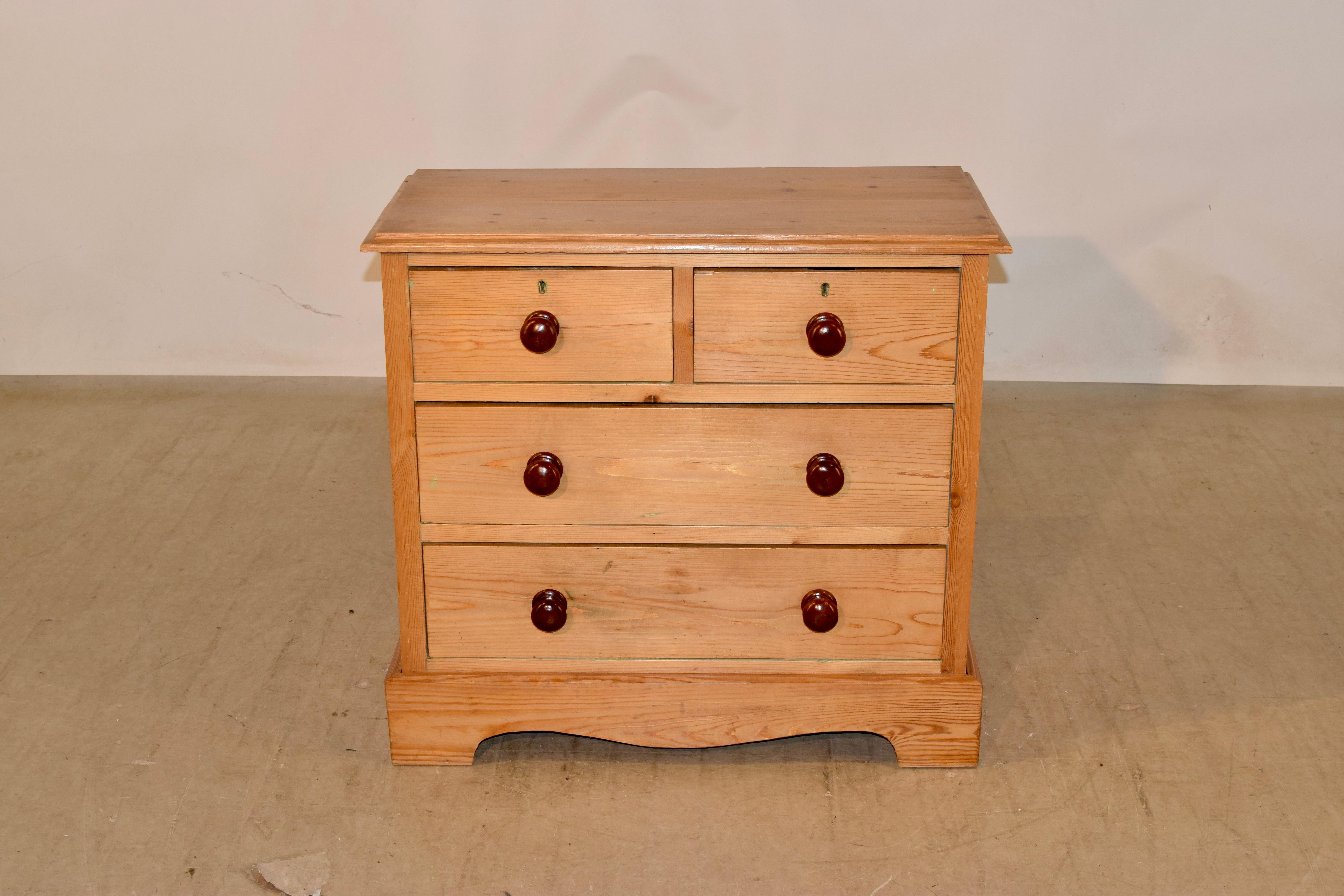 19th century small pine chest of drawers from England with a stacked beveled edge around the top. The case has simple paneled sides and contains two over two drawers in the front, over a scalloped and banded base.