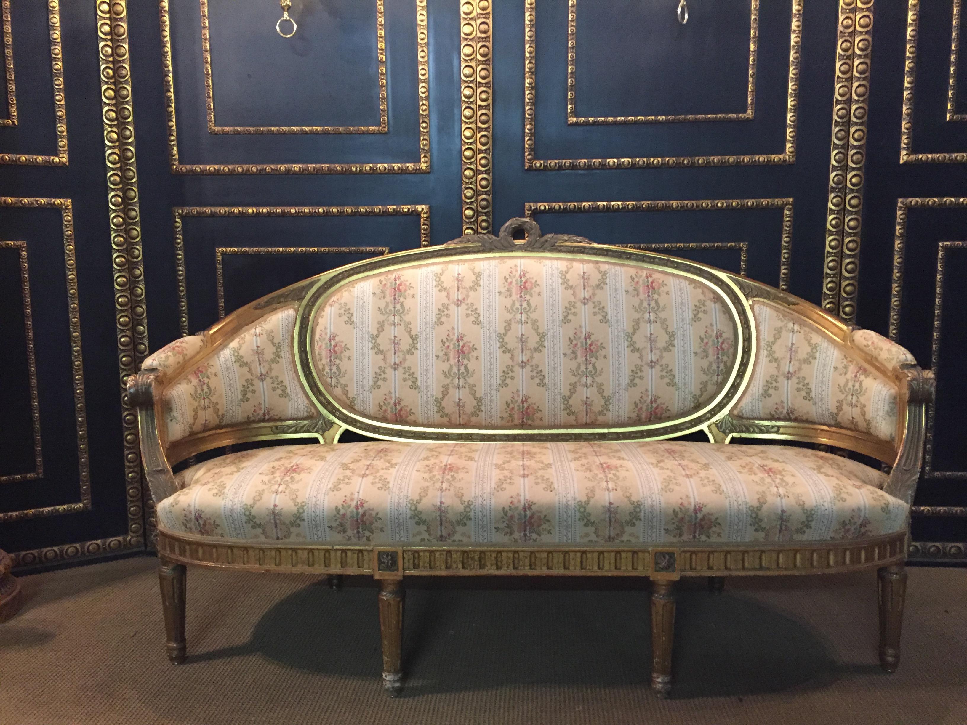 Solid beechwood, finely carved, poliment gilded and partial sheet gilded. Cambered and carved frame on carved, tapering legs. Curved armrests. Flanked by relieved leaf rosettes. Rising armrests in medallion-shaped back frame with carved crown
